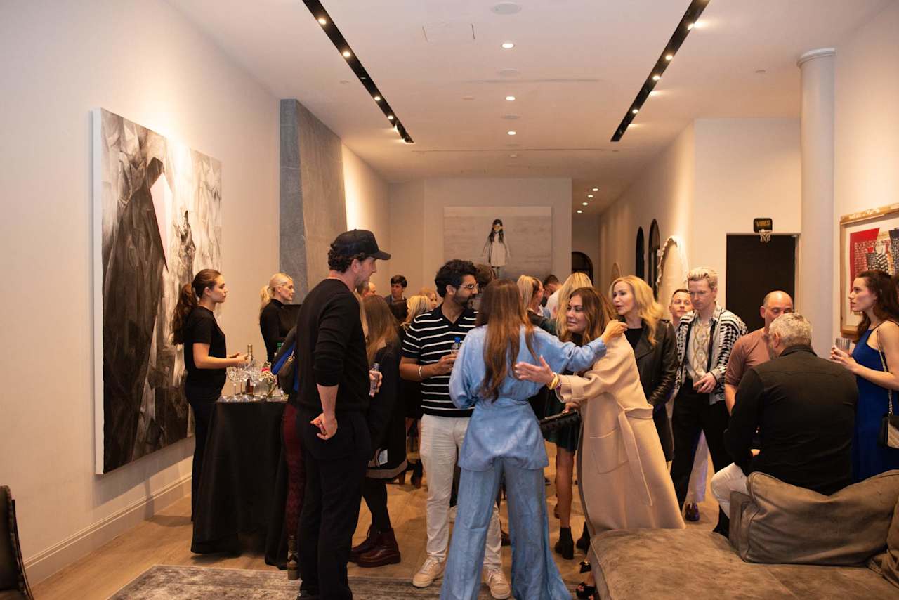 Guests mingle at a reception beside large artworks and a refreshments table.
