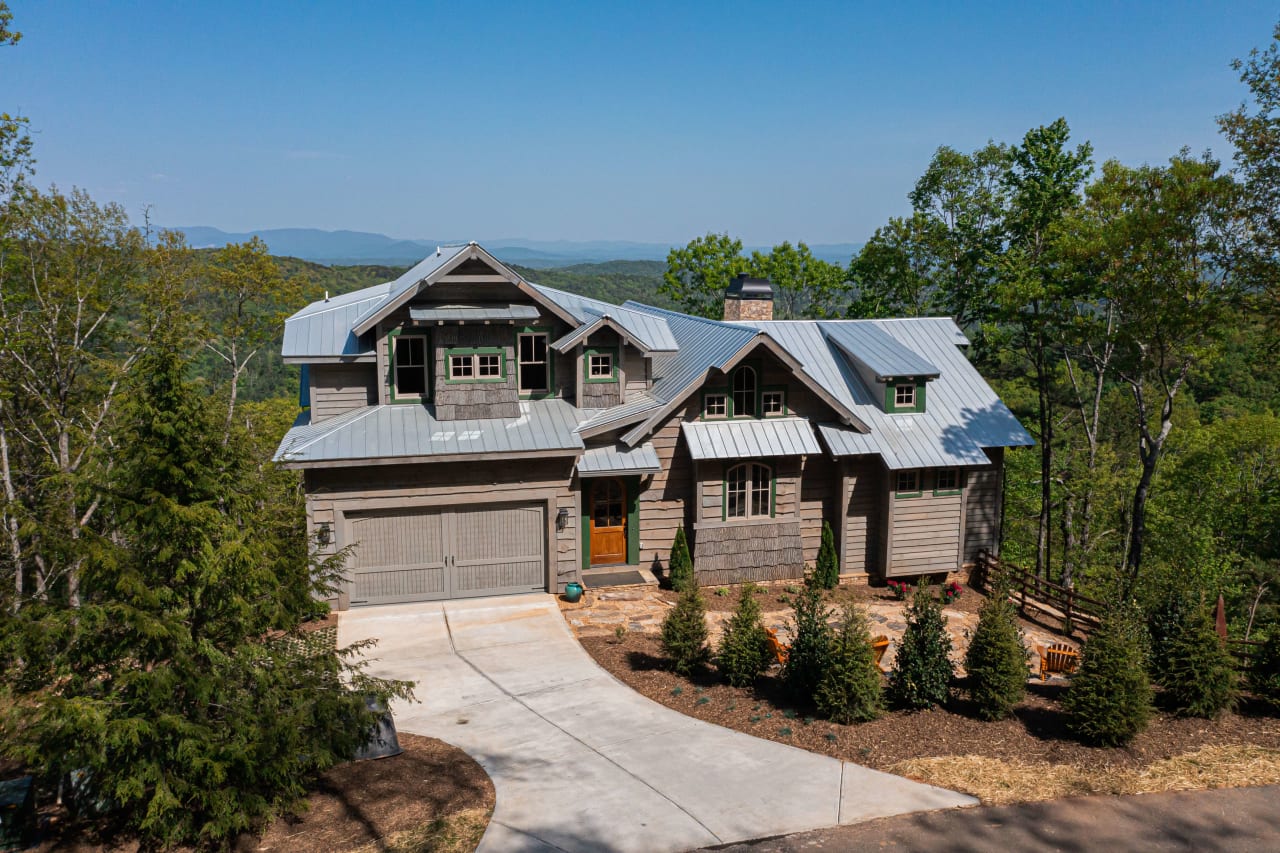 A large house with a garage and driveway sits on a hill surrounded by trees.