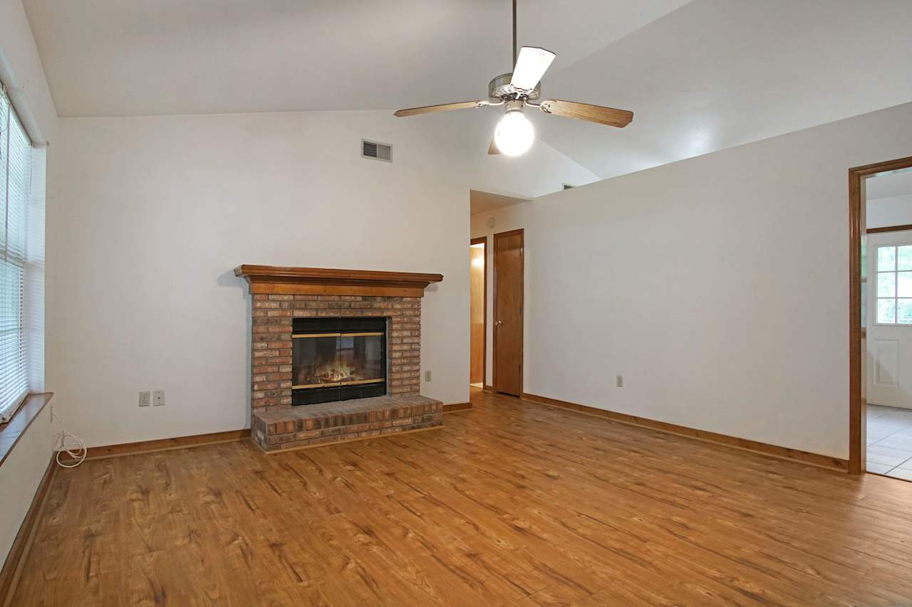 Photo of main living area centered around a brick fireplace with vaulted ceilings, plank floors, and a fan light fixture