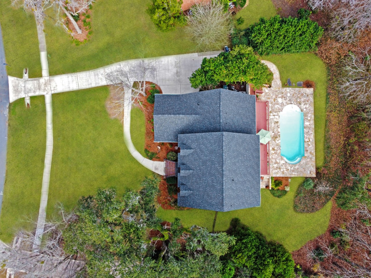 An aerial view of a house with a swimming pool in the backyard, surrounded by a landscaped garden.