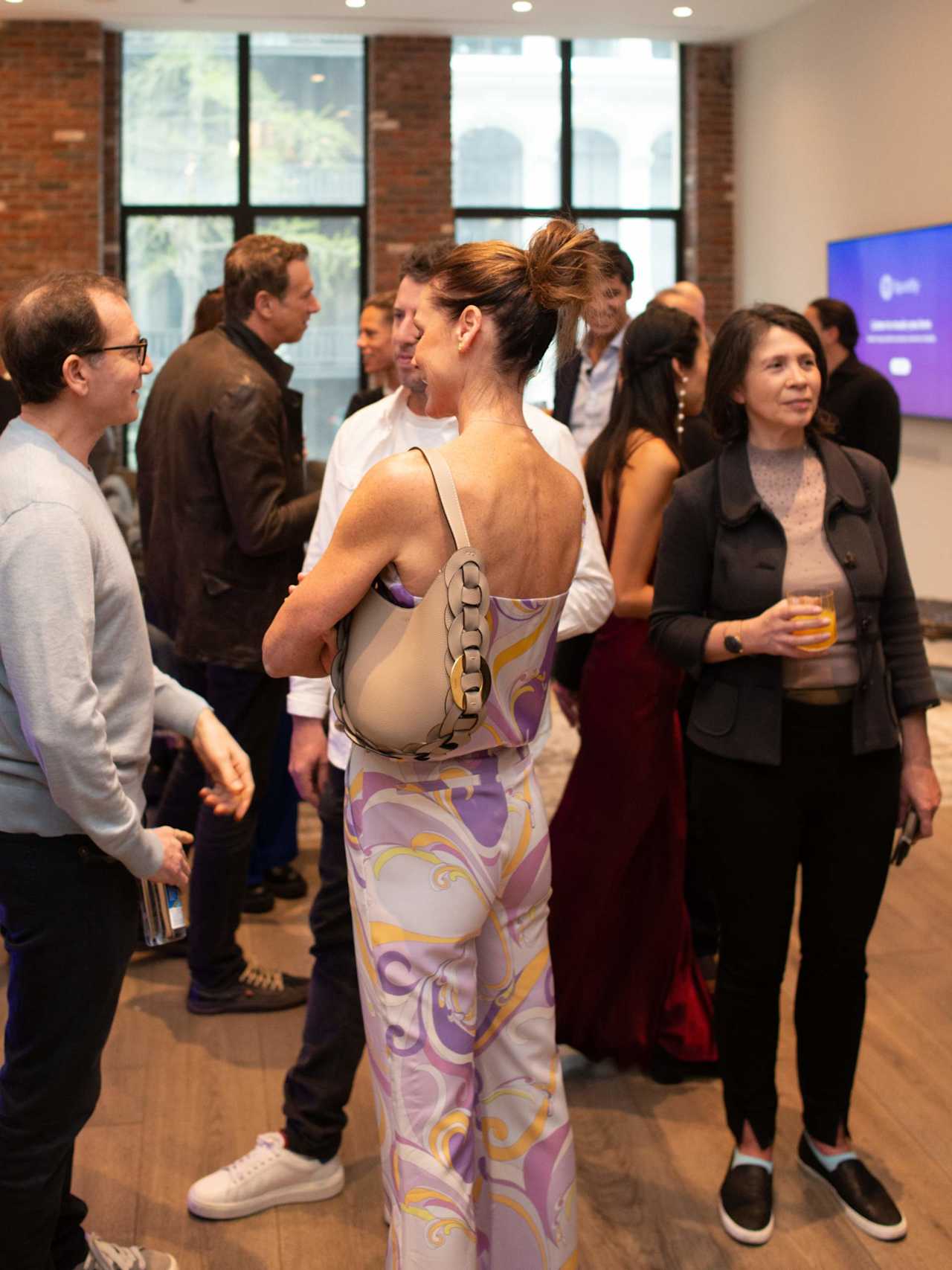 Guests mingle at a networking event, with a woman in a patterned dress in the foreground.