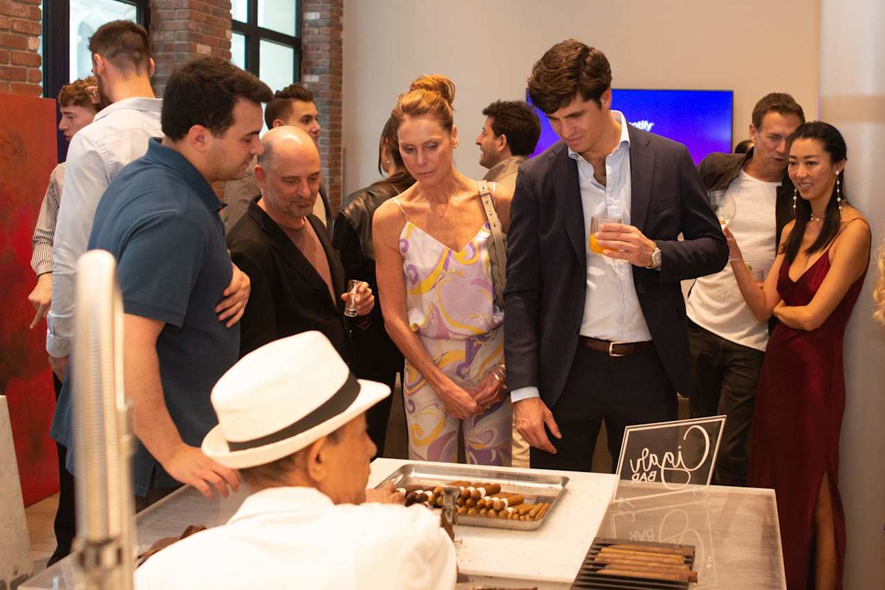 Guests gather around a chef serving pastries at an indoor event.