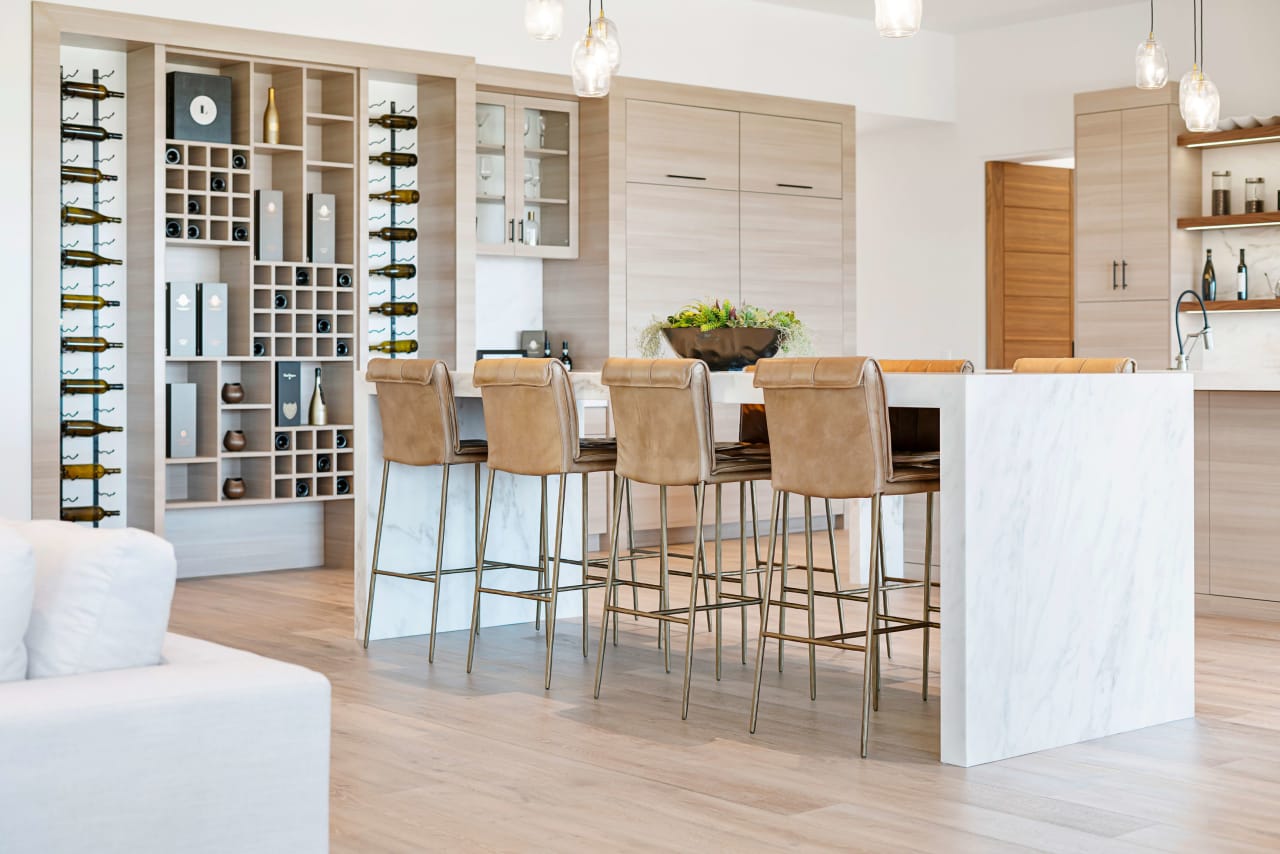 A modern kitchen with a breakfast bar made of white marble beside a wine rack.