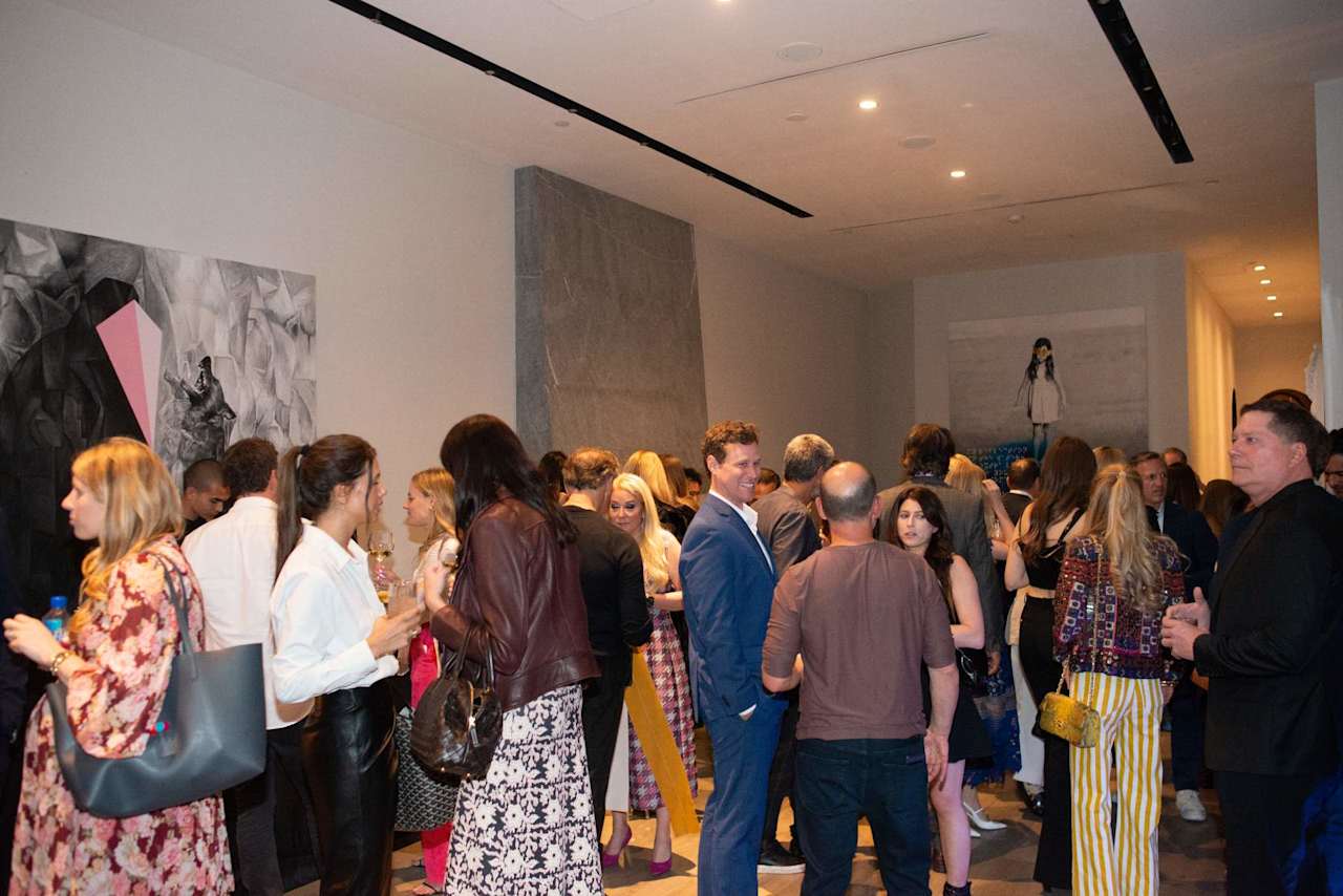 Guests mingle at a crowded reception in a modern gallery with contemporary artwork.