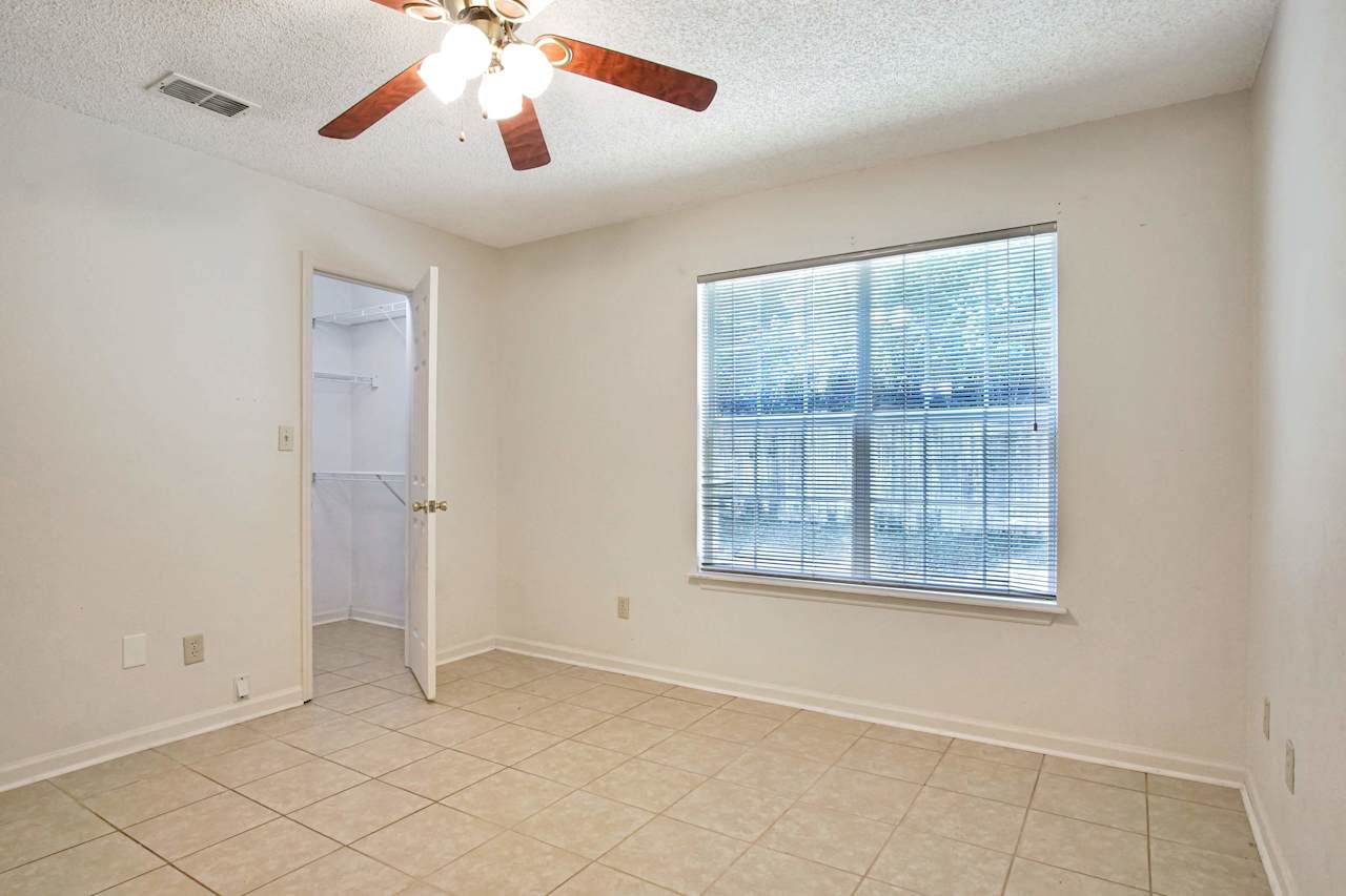 Photo of the primary bedroom featuring lightly colored walls, lightly colored tiled floors, access to the walk-in closet with built-in shelving, and a large window with white blinds  at 2709 Oak Park Court, Tallahassee, Florida 32308