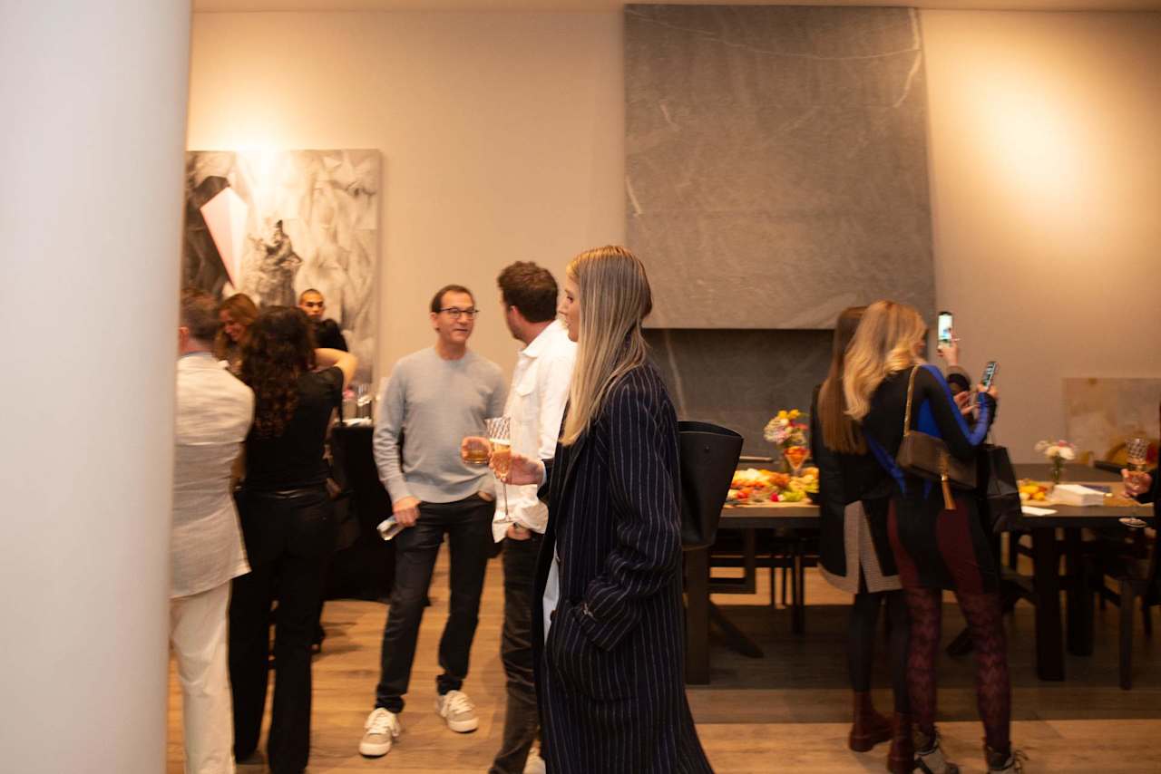 Guests mingle at an indoor event as a woman in a dark pinstriped suit holds a drink.
