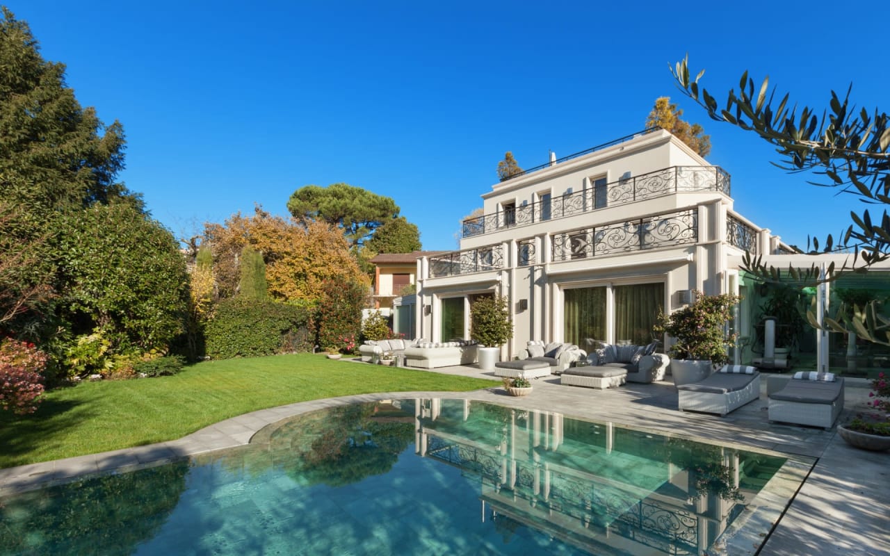 A large white house with large windows and a crystal clear pool on a sunny day.