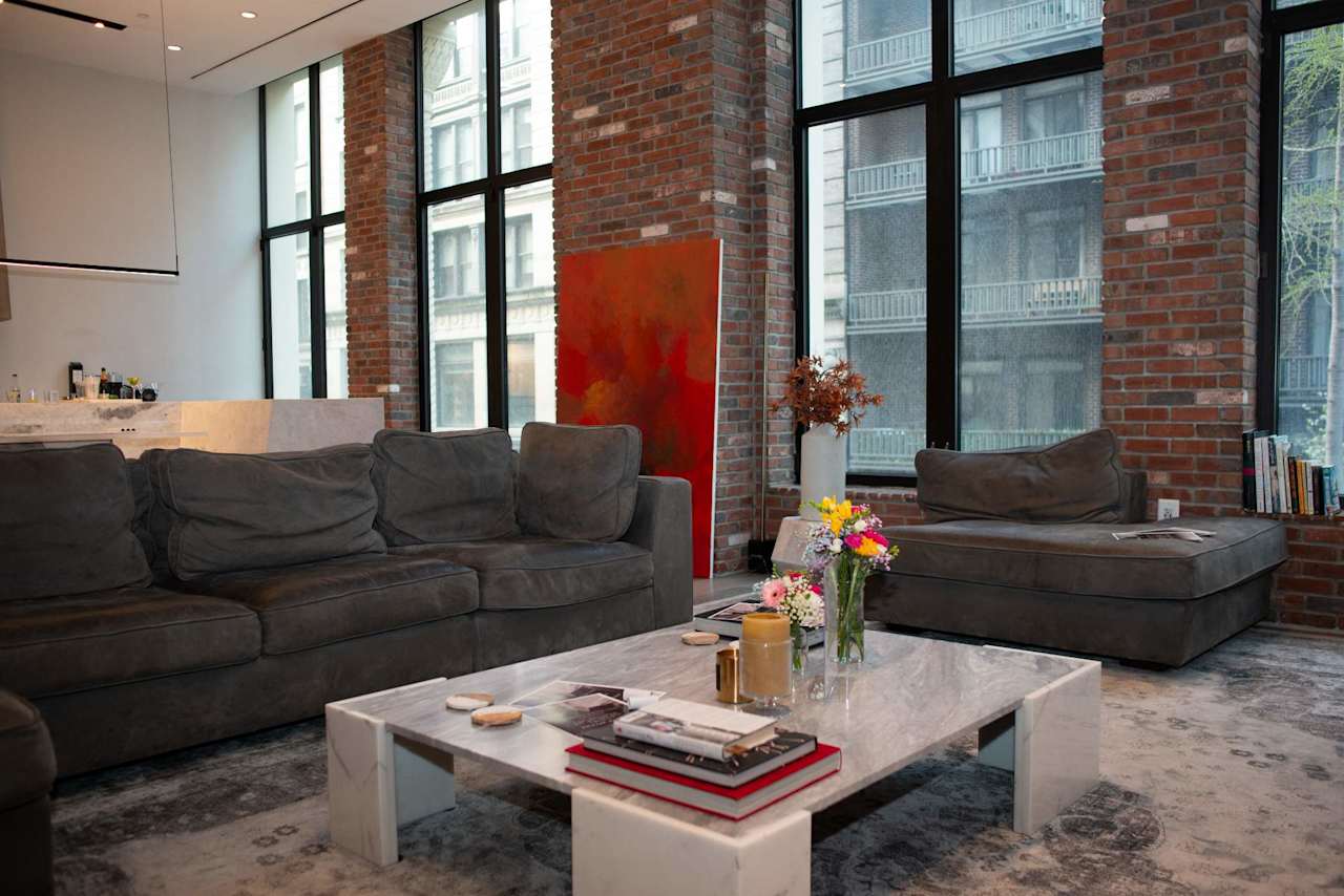 Loft living room with exposed brick, tall windows, a gray sectional, and a marble coffee table.