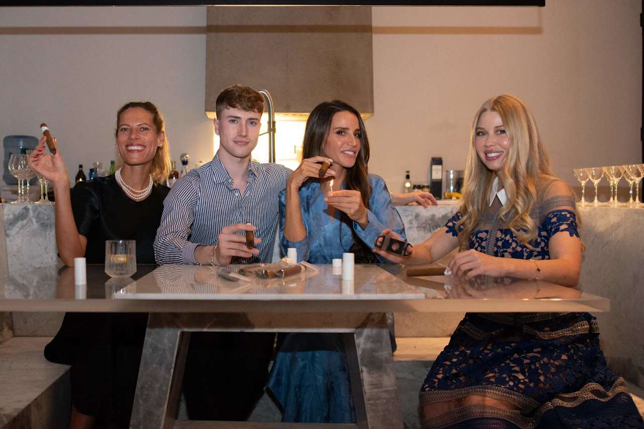 Four people smile together at a marble kitchen island, holding drinks.