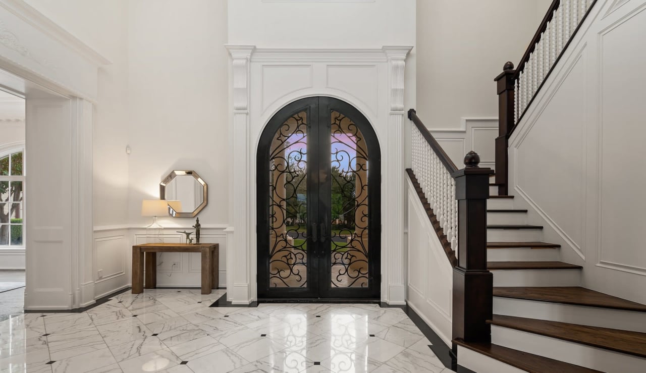 An elegant foyer with a staircase and a wrought iron door.