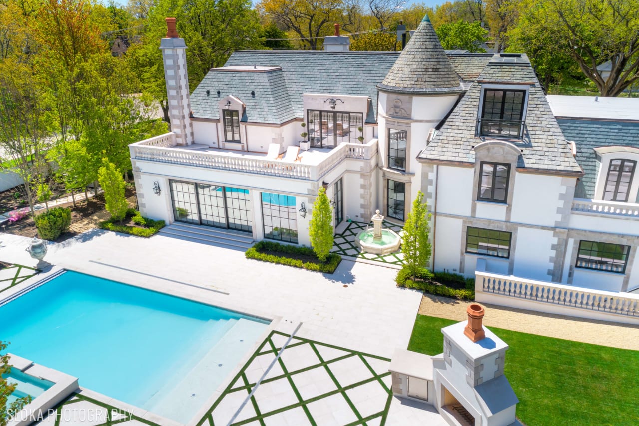 Aerial view of a large, white mansion with a swimming pool and fountain in the backyard