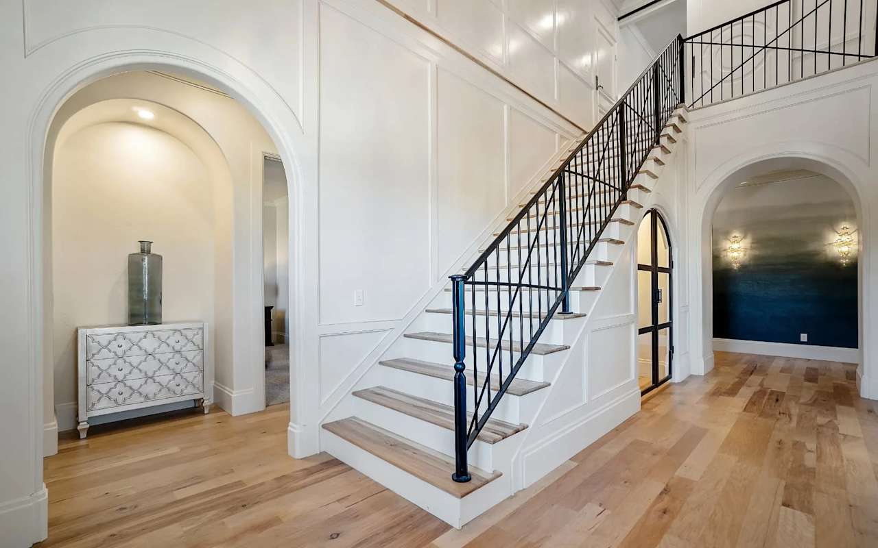 A hallway with a wooden staircase that has a black railing.