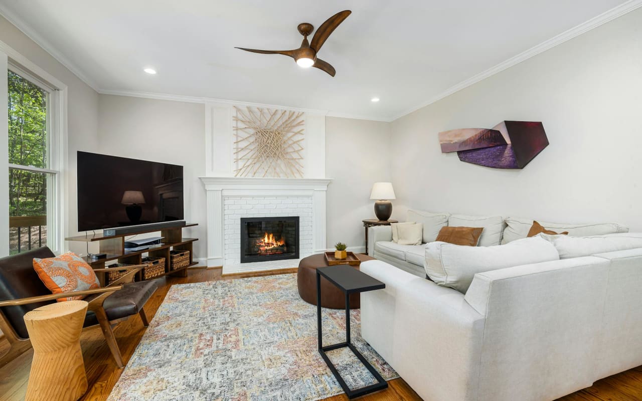 Modern living room with a wall-mounted flat-screen TV above a fireplace, a cozy couch, a black armchair, and a window.