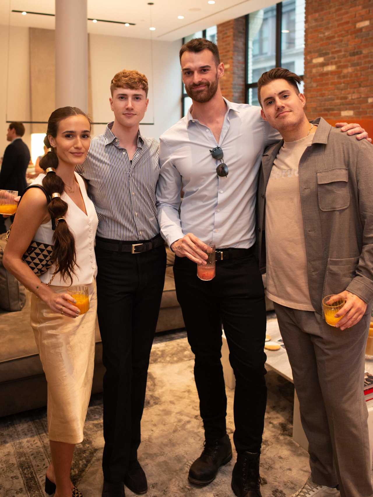 Four people pose together with drinks at an office gathering.