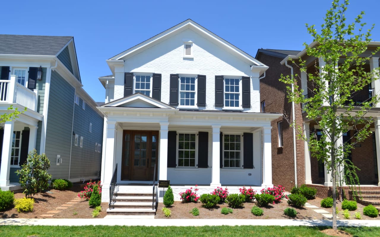 A two-story Colonial-style white house with a flower and plant box, a front porch with railings, a walkway, and a front lawn.