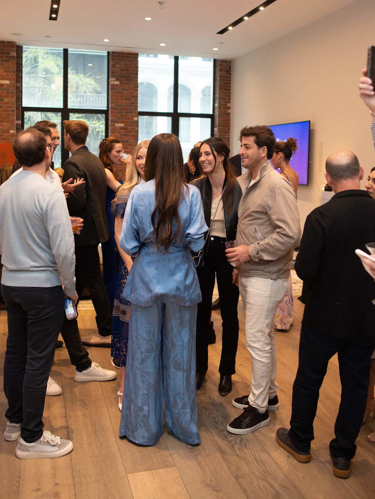 Guests mingle at an indoor event, including a woman in a blue patterned outfit.