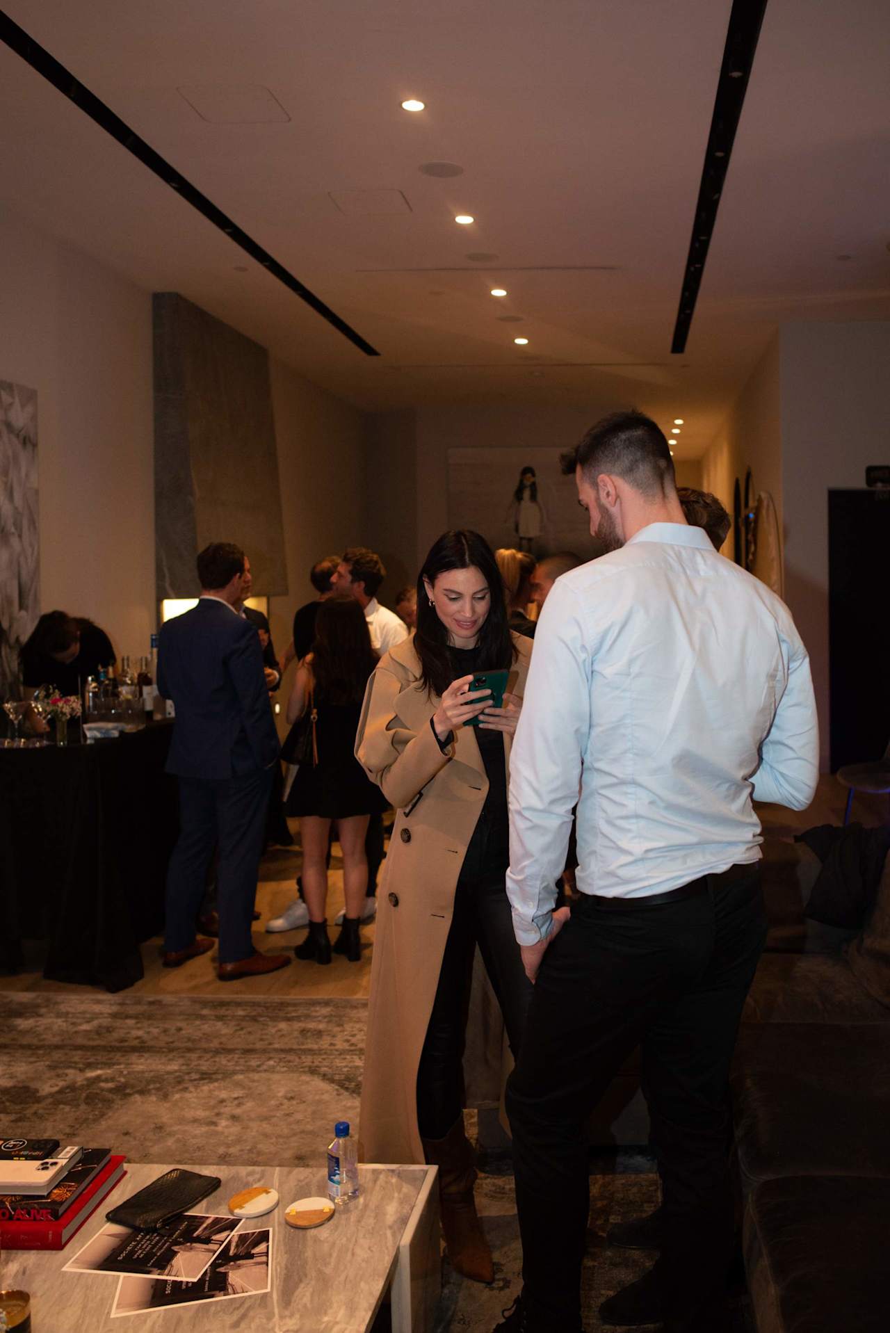 Guests mingle at a Societe Real Estate event as a woman checks her phone.