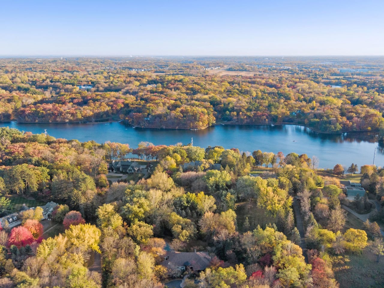 An aerial view of houses near a calm lake surrounded by lush green trees.