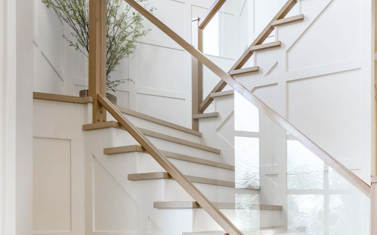 A close-up of a staircase with a glass railing and green plant