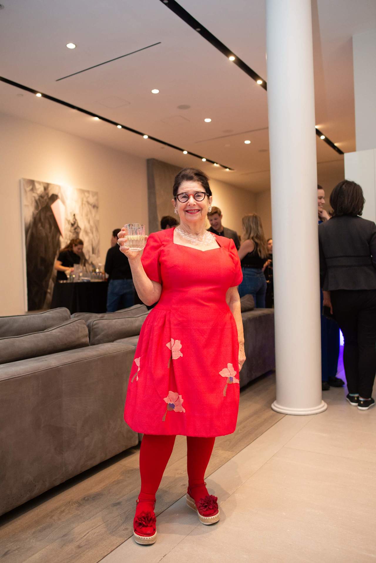 Woman in a bright red floral dress raises a glass at a reception.