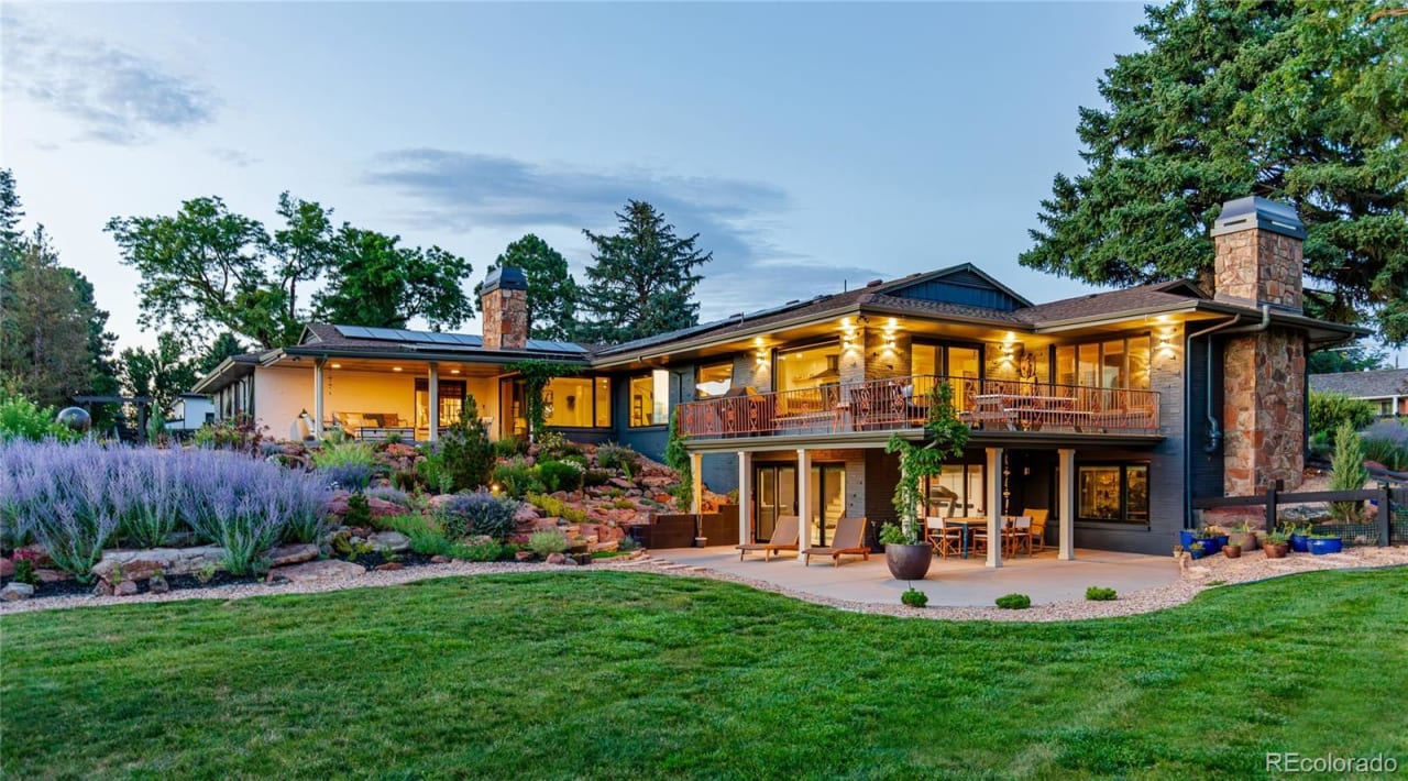 A large, two-story house with a red roof and white siding sits on a lush green lawn