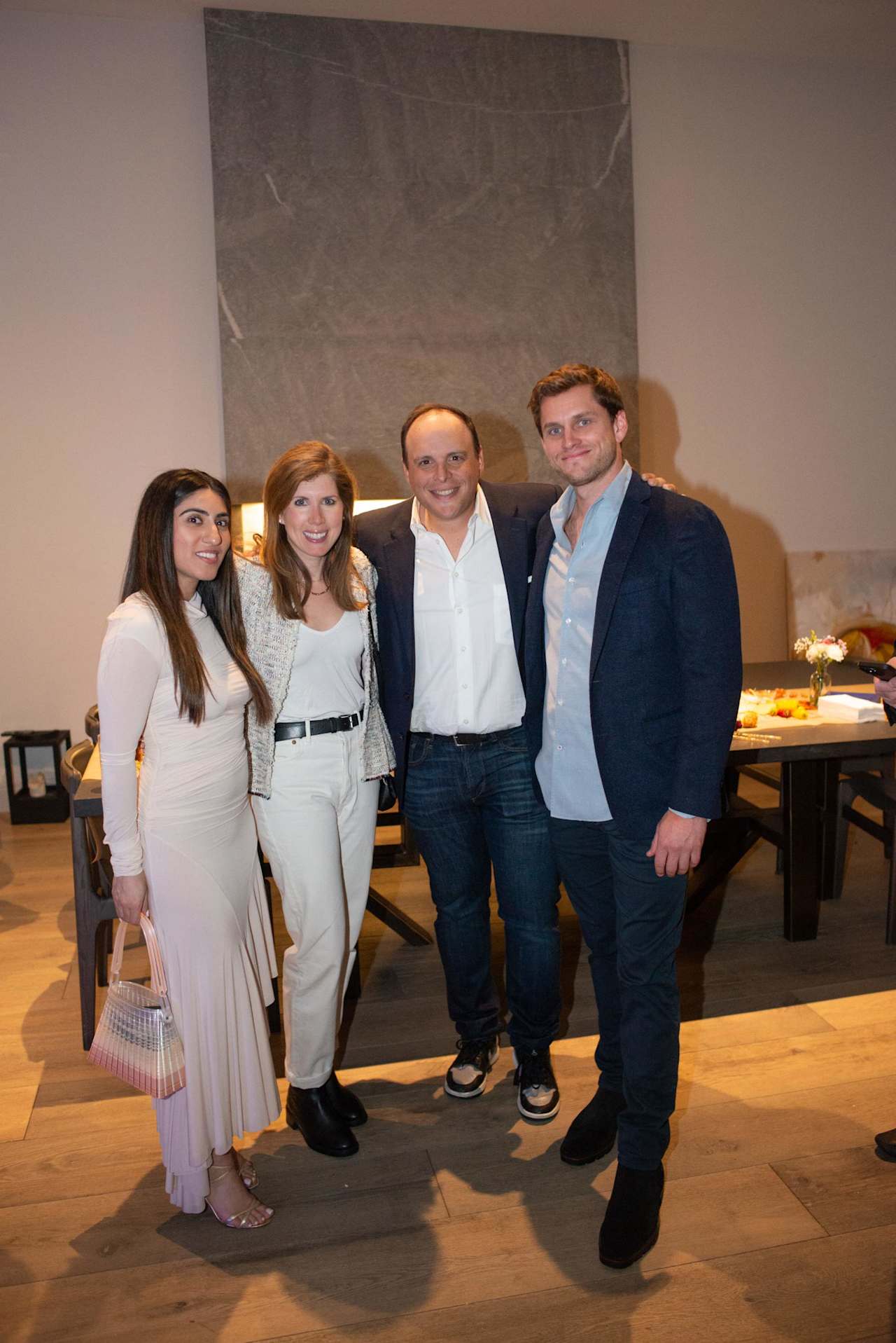 Four adults pose together at an indoor event, with a large stone wall behind them.