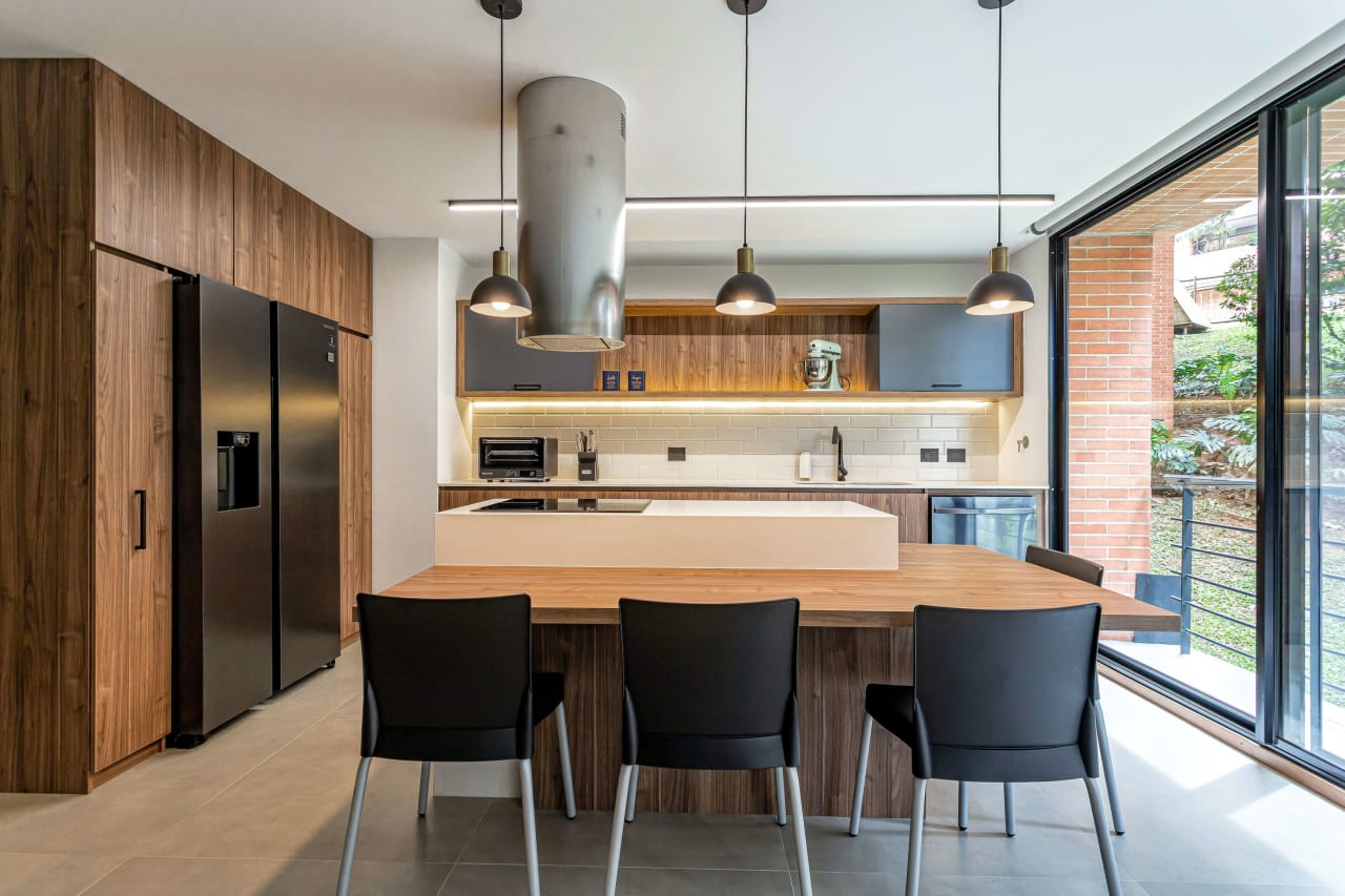 A modern kitchen with a light colored wooden table and four black chairs. 