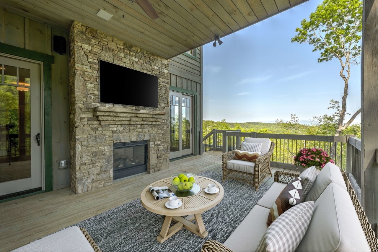 A covered patio with a stone fireplace and a flat screen TV mounted on the wall above the fireplace.