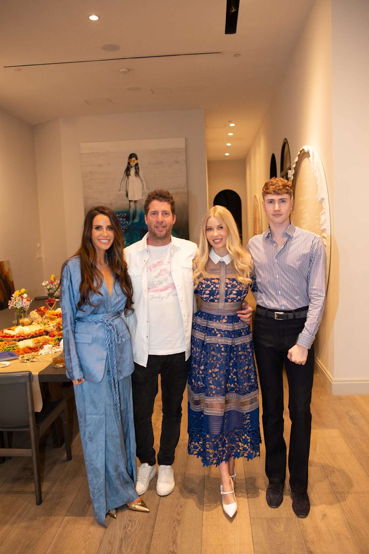 Four people pose at an indoor event beside a buffet table and wall artwork.