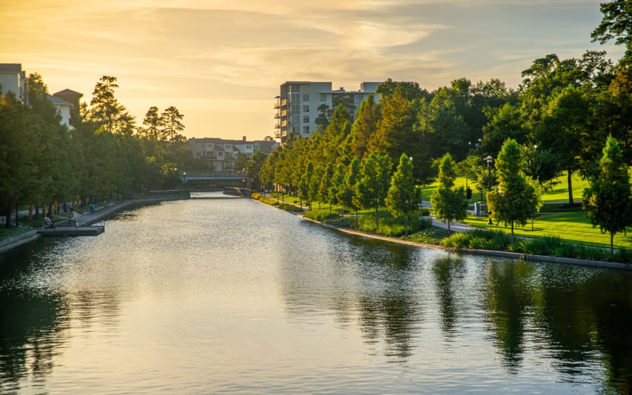 A waterway surrounded by trees and distant residential buildings of varying heights.