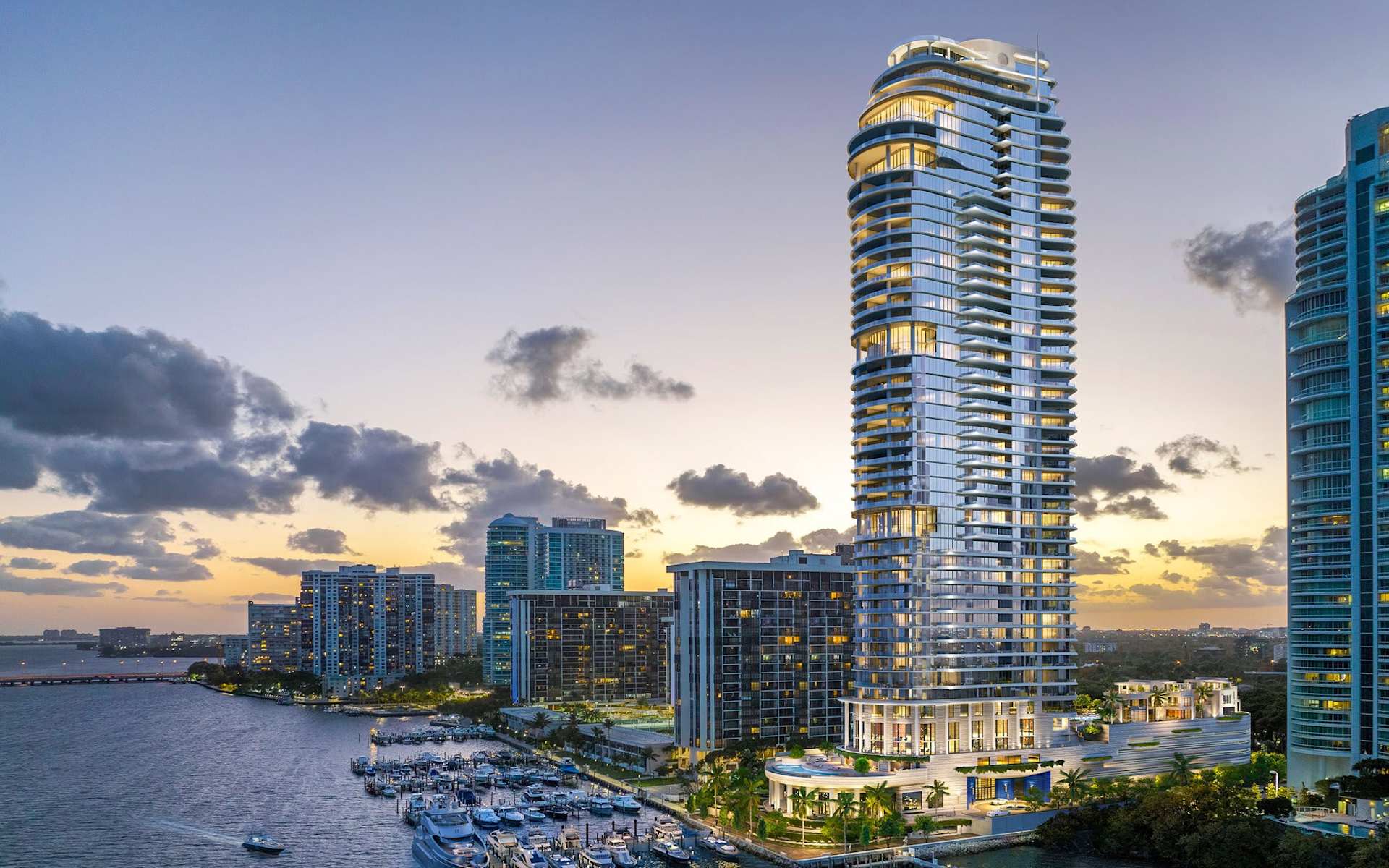 St. Regis Miami Residences tower overlooking a marina, with curved balconies and the city skyline at dusk.