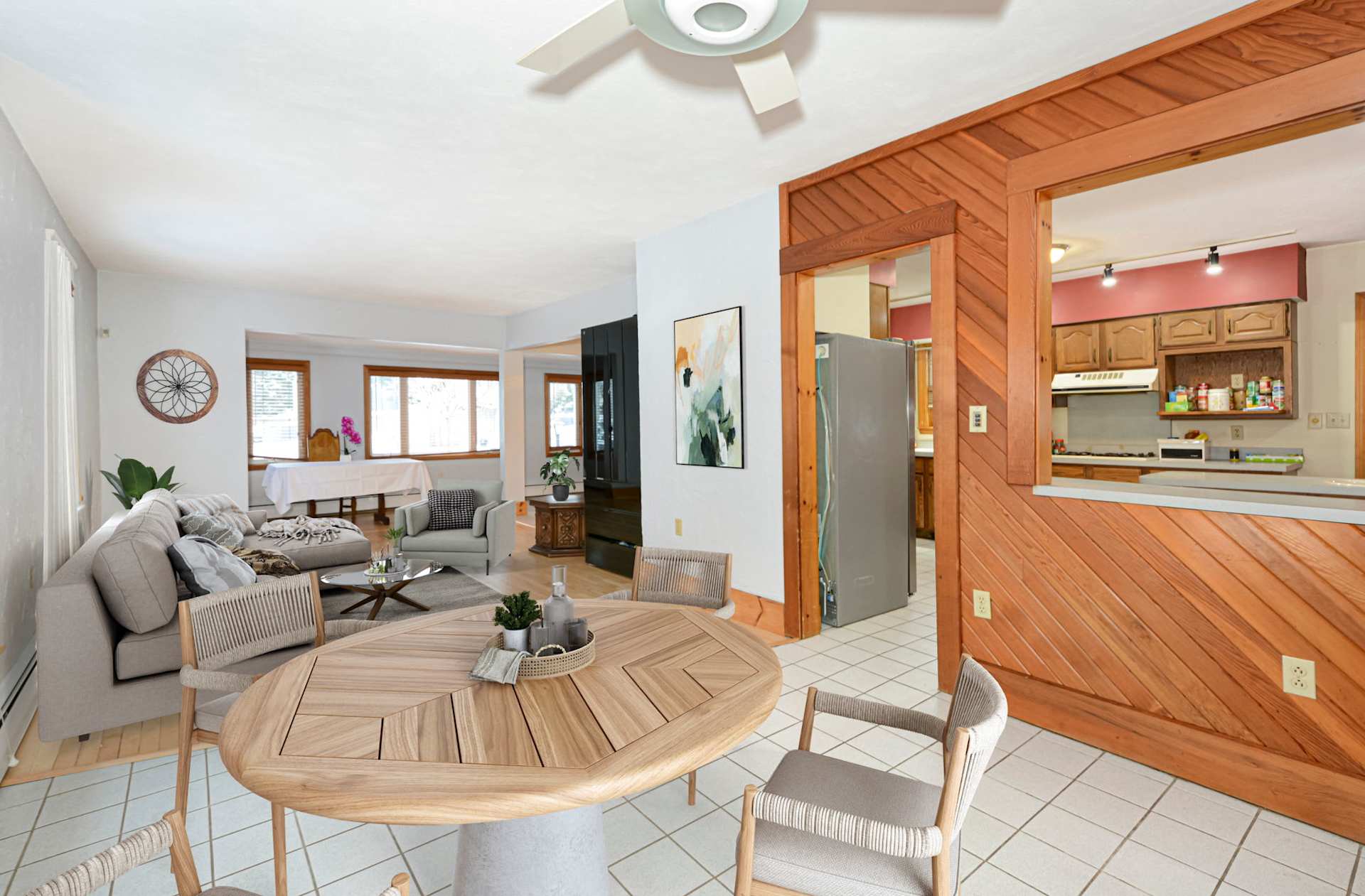 Open-plan living and dining area with a gray sectional and wood-paneled kitchen opening.