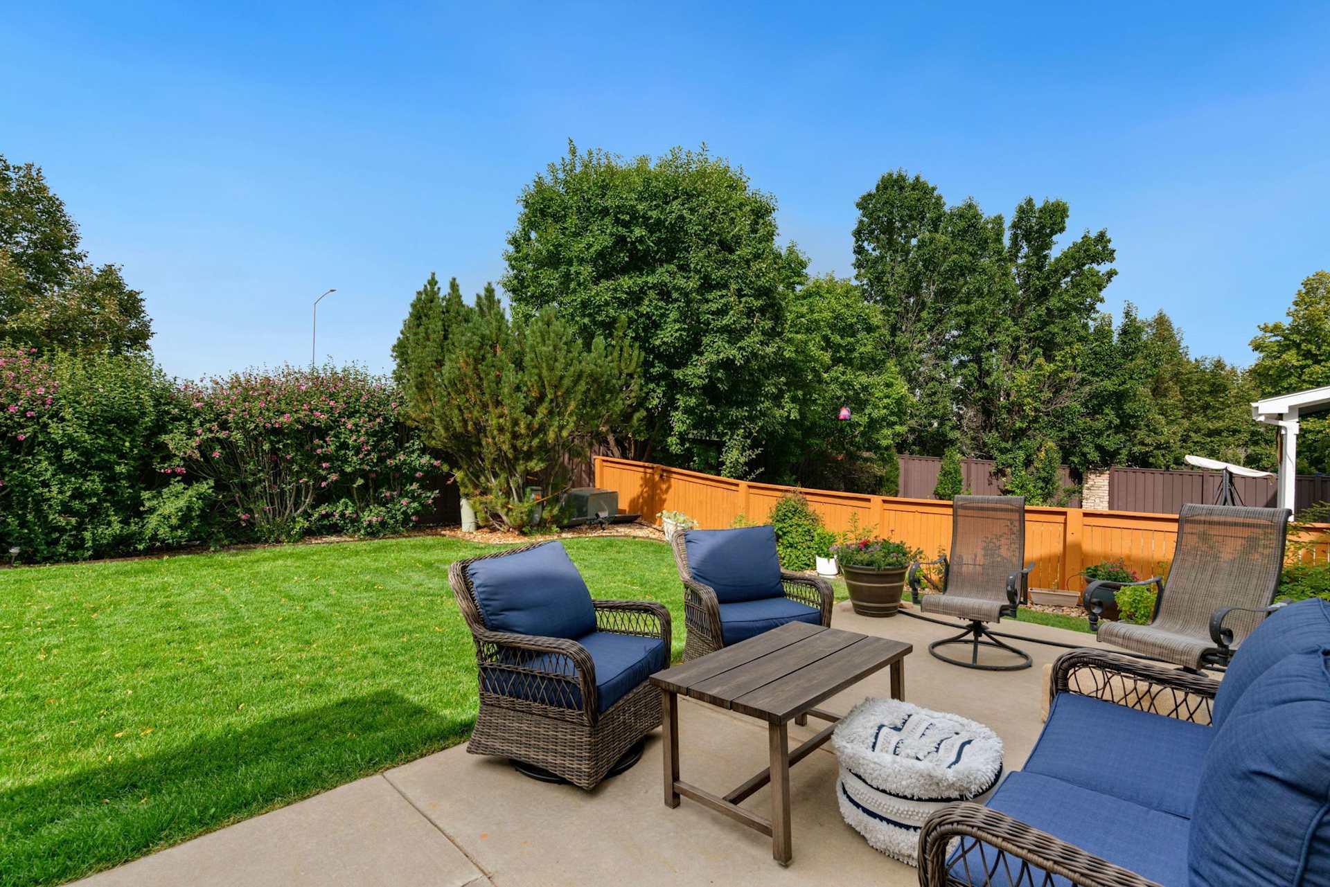Backyard patio with wicker seating, a green lawn, and an orange fence.