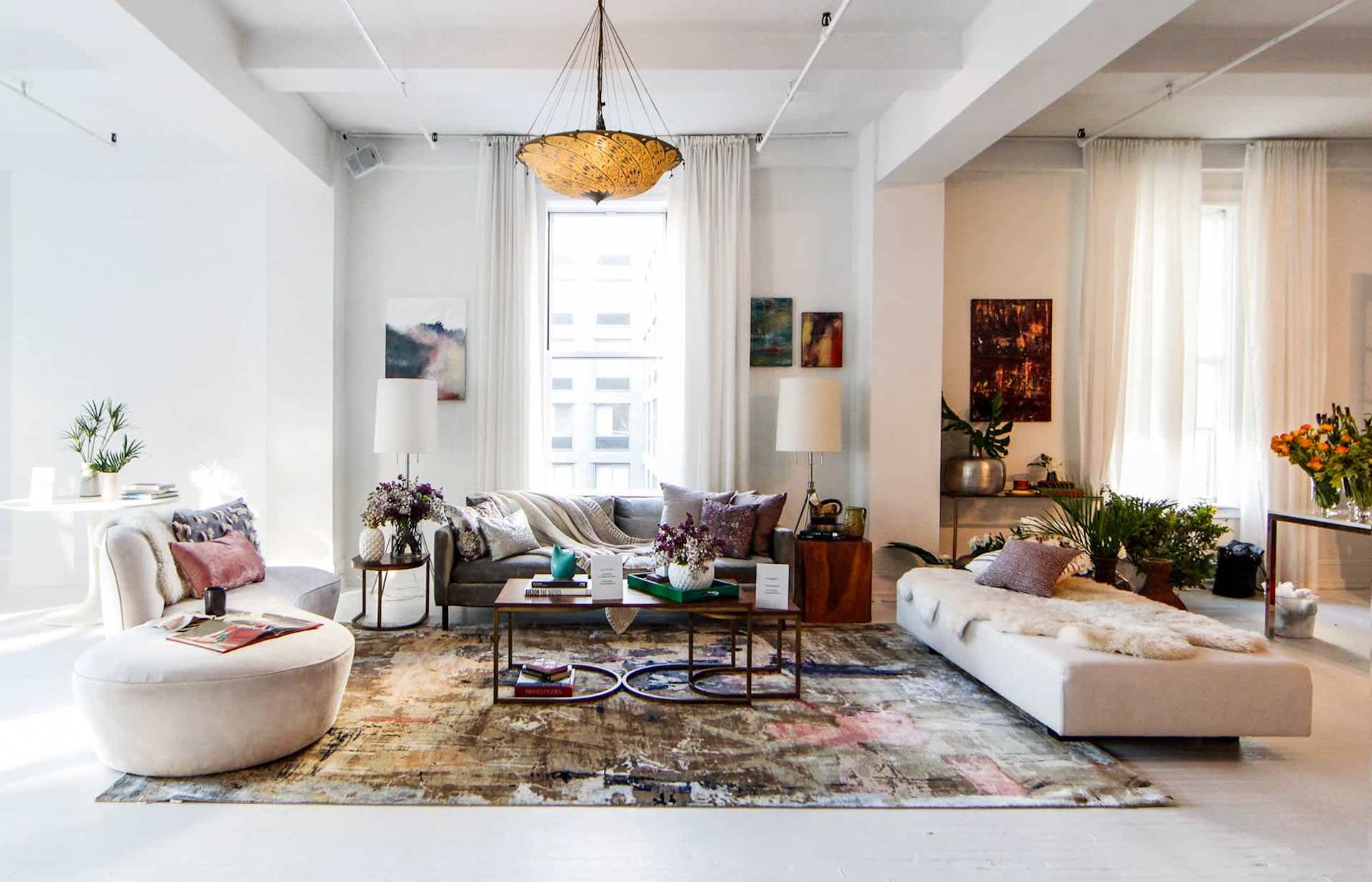 Bright living room with tall windows, layered seating, a patterned rug, and an amber pendant light.