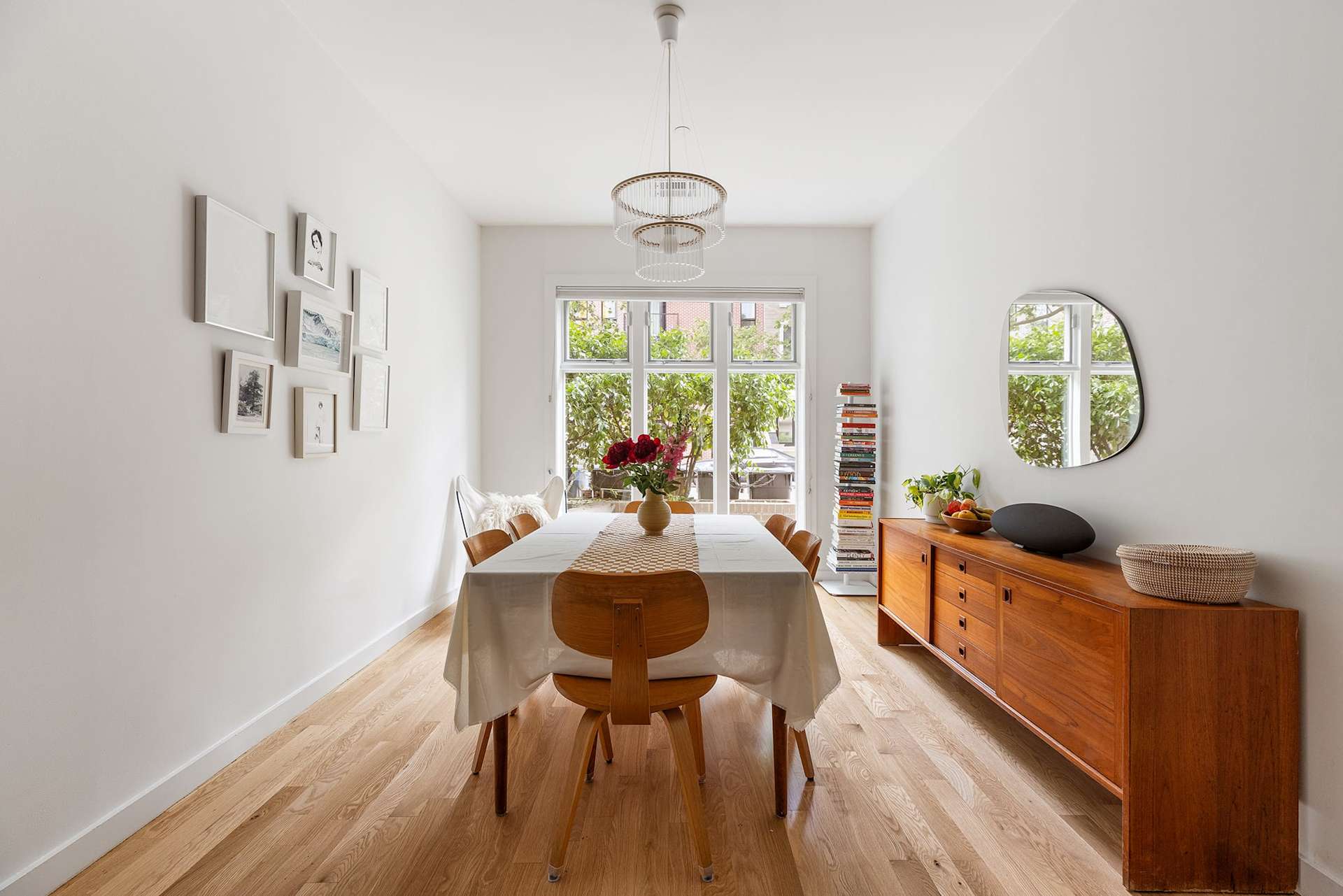 Bright condo dining room with a wood dining set and leafy greenery visible through large windows.