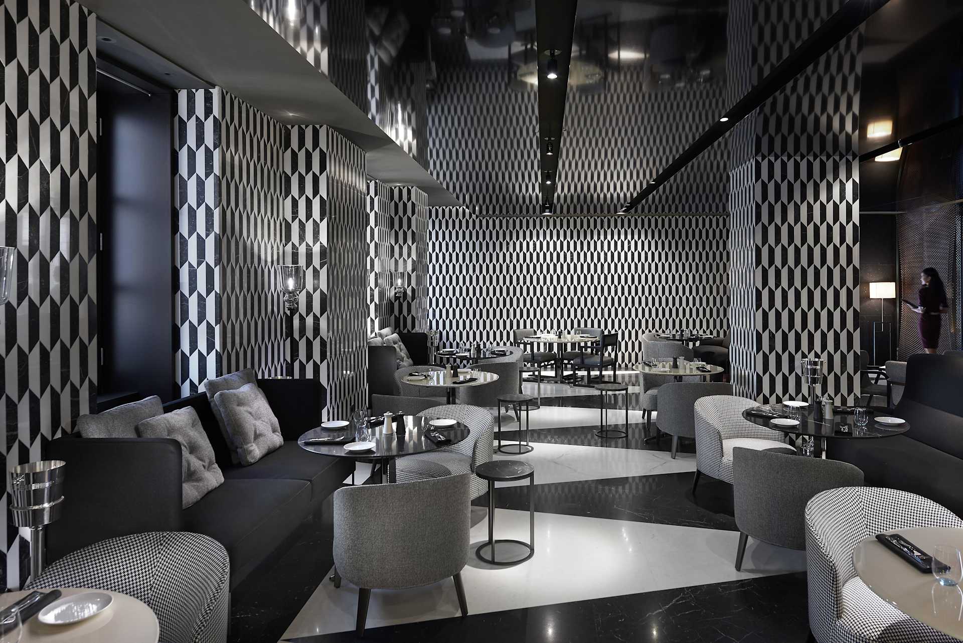 Furnished lounge with geometric black-and-white walls, gray seating, and small tables.