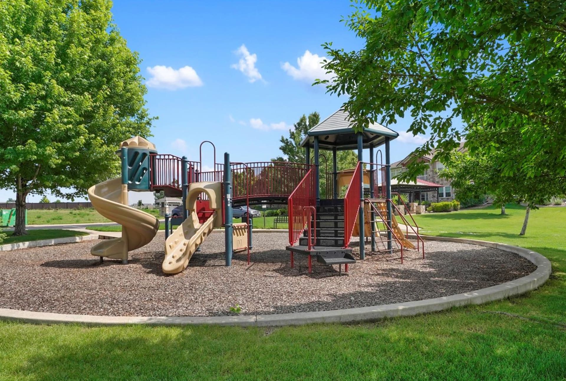 Neighborhood playground with multilevel slides and play structure beneath mature trees.