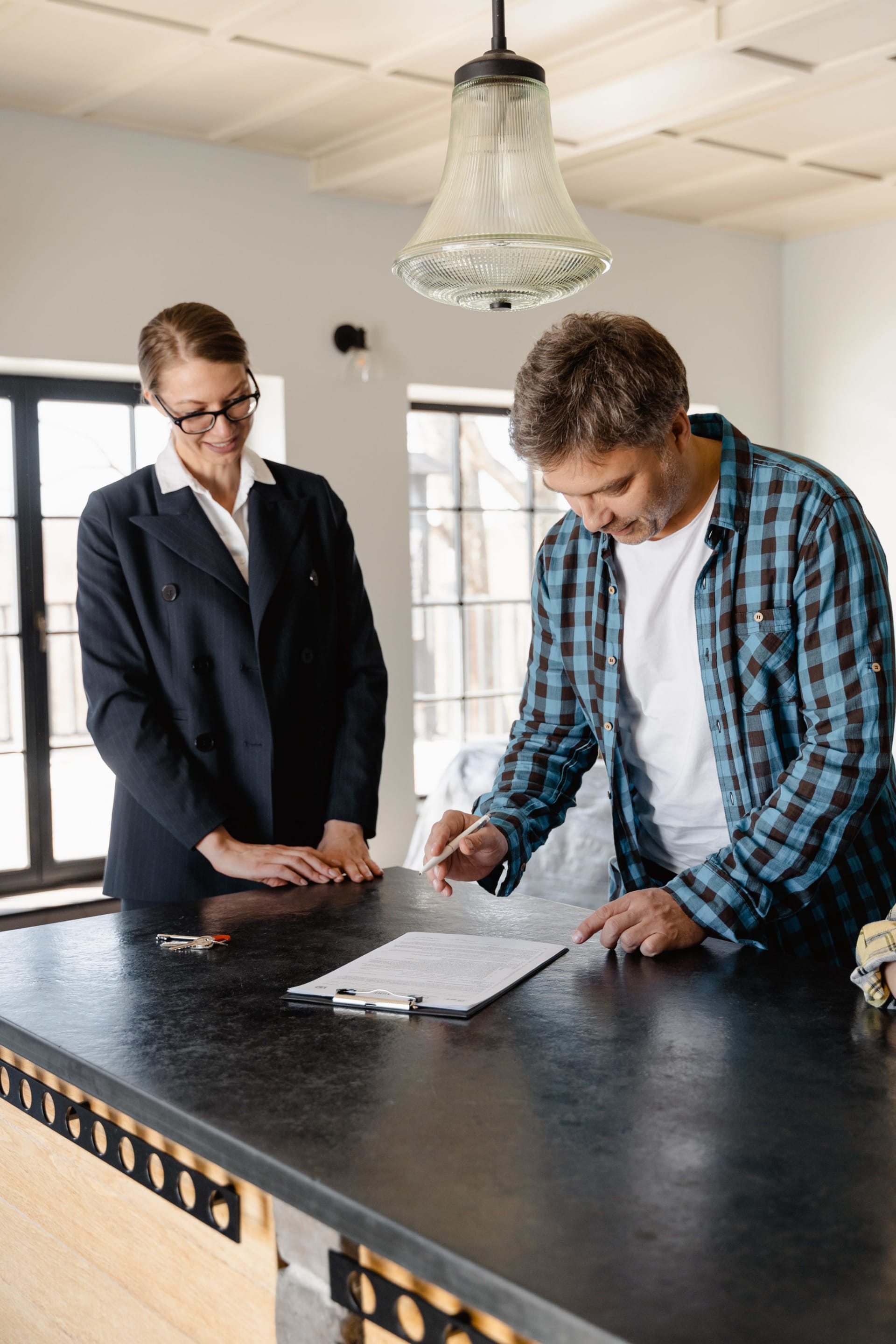 A female real estate agent attentively observing as a man prepares to sign a document