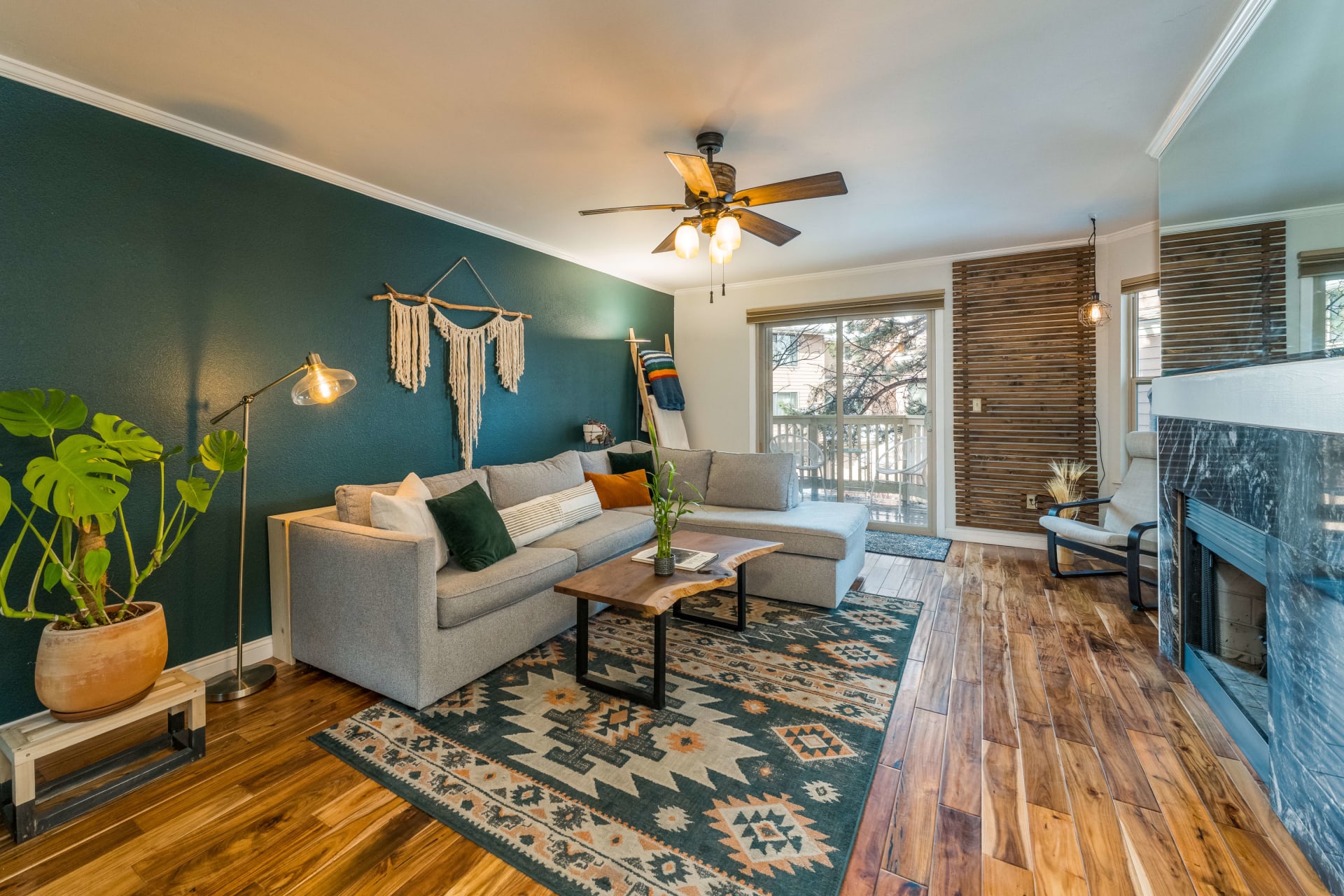 living room with a dark green wall that has a grey couch pushed against it, a natural wood coffee table sit atop an aztec print rug 