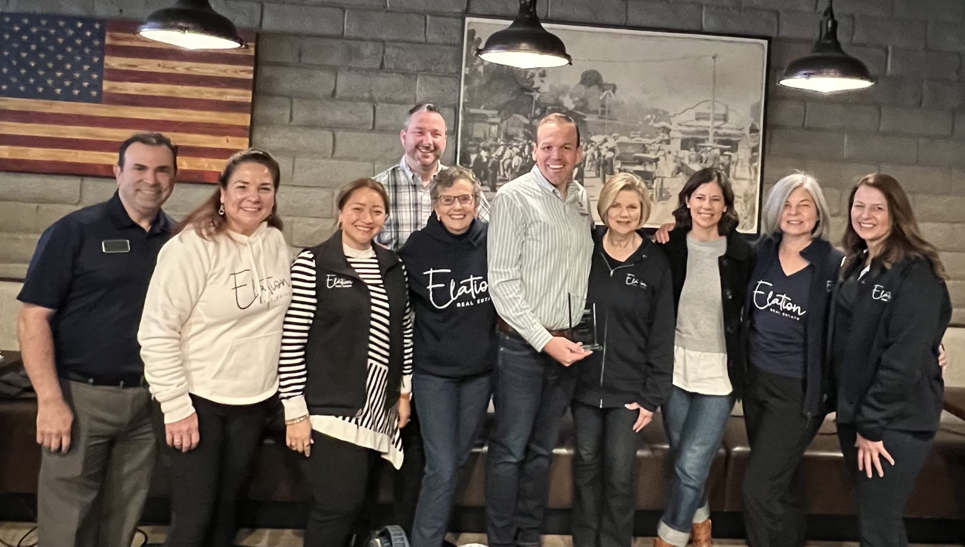 Ten smiling real estate agents pose together; the man near the center holds an award.
