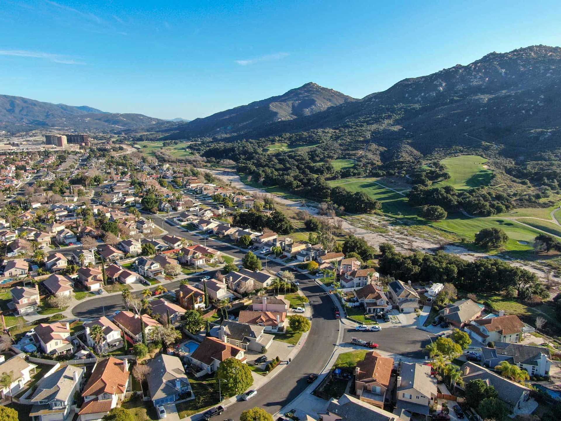 Aerial view of a residential neighborhood beside a golf course and rugged mountains.