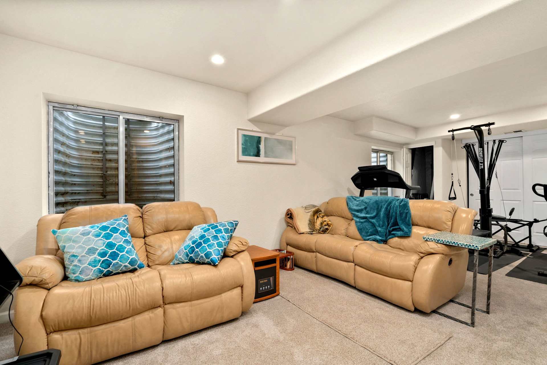 Basement recreation room with tan leather sofas and a treadmill beside a weight machine.