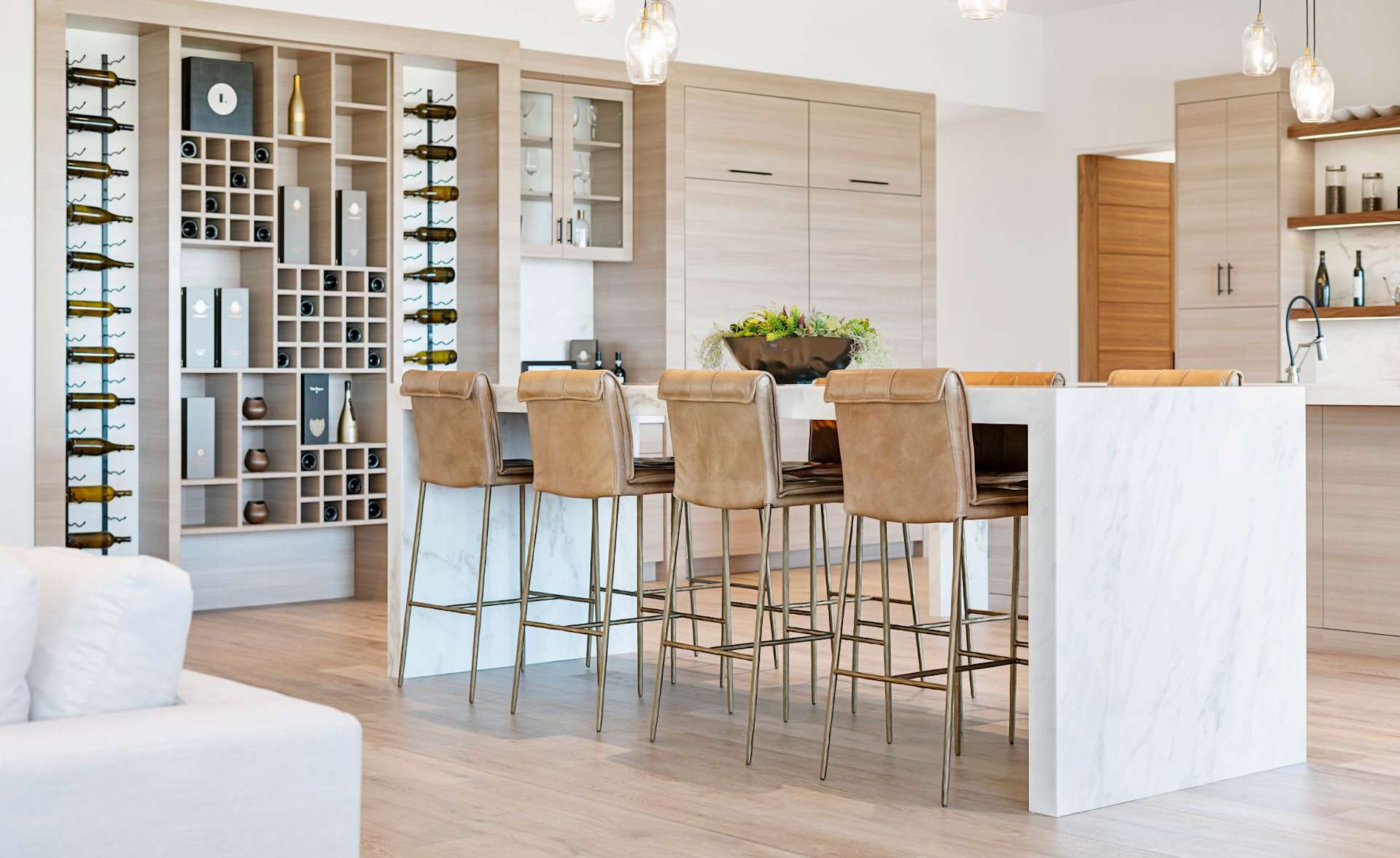 Modern kitchen with a marble island, leather bar stools, and built-in wine display.