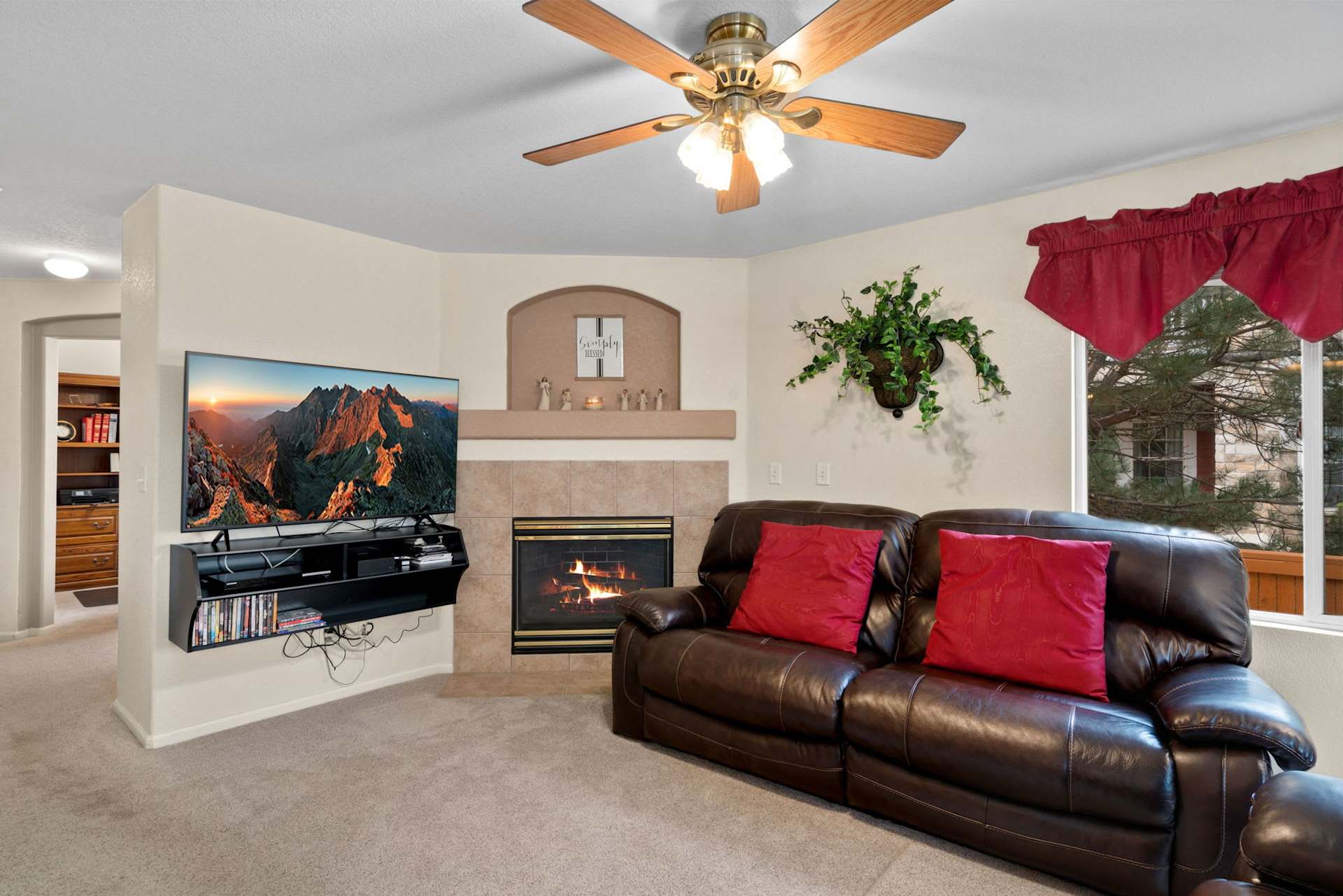 Living room with a leather sectional, red pillows, and a lit fireplace beneath a wall-mounted television.
