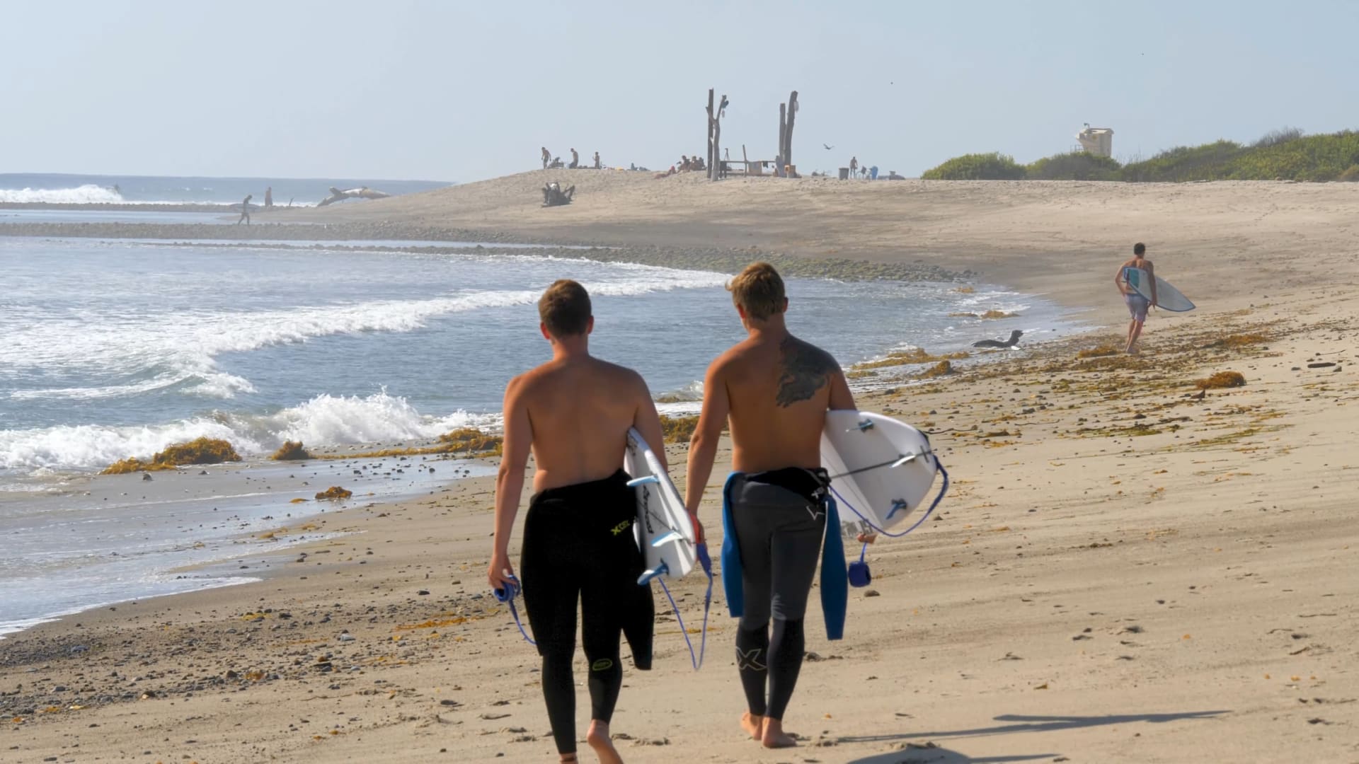 Two boys carrying surfboards walking on the sand along the ocean water