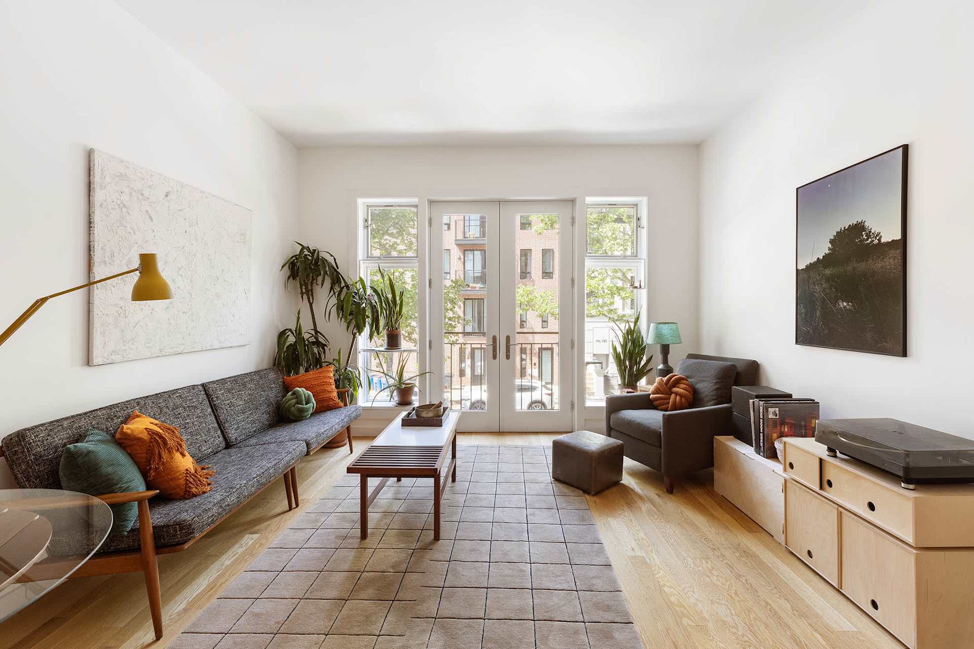 Bright living room with high ceilings, gray seating, plants, and French doors opening to Juliette balconies.