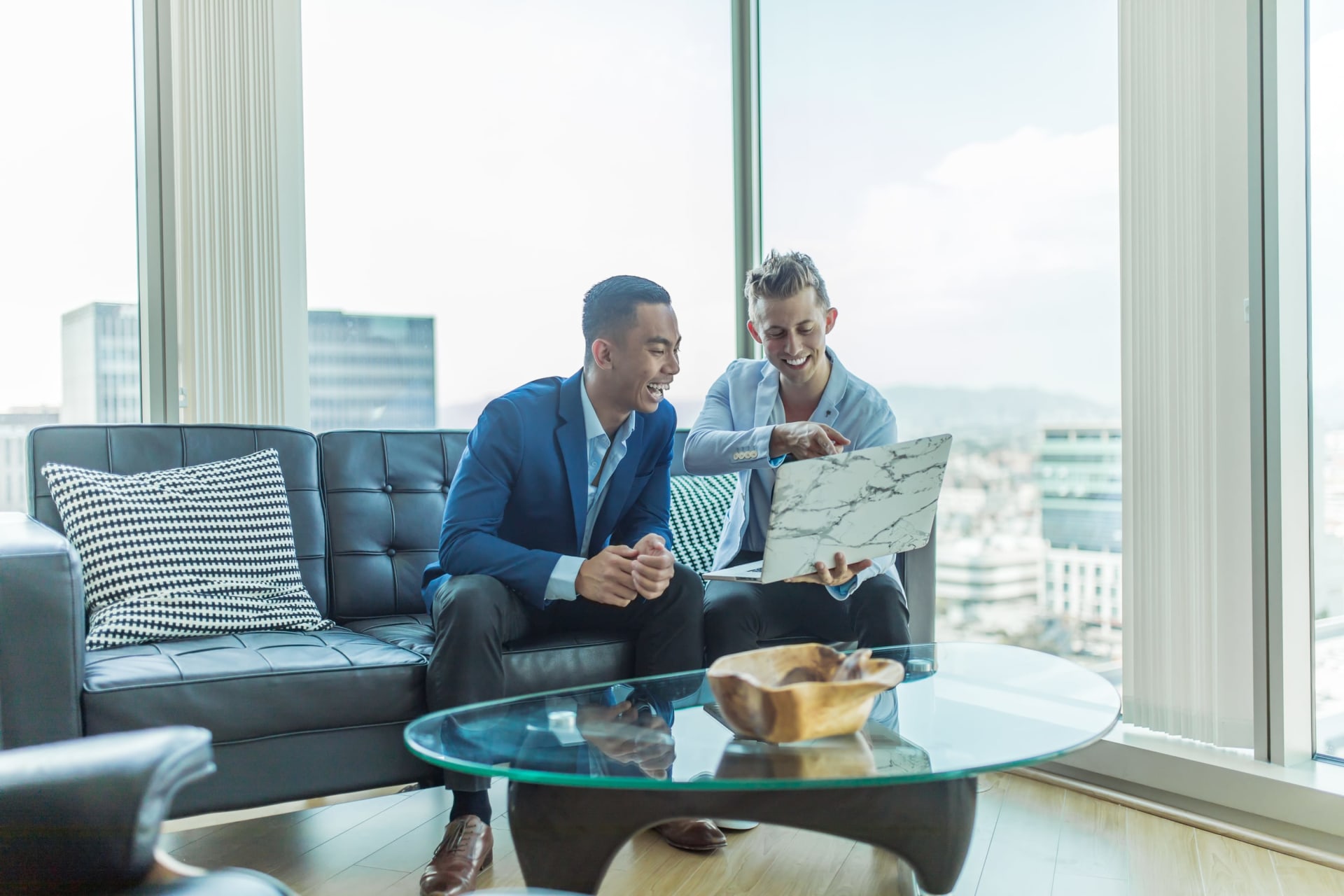 Two real estate professionals sharing a moment of laughter, with one holding a laptop.