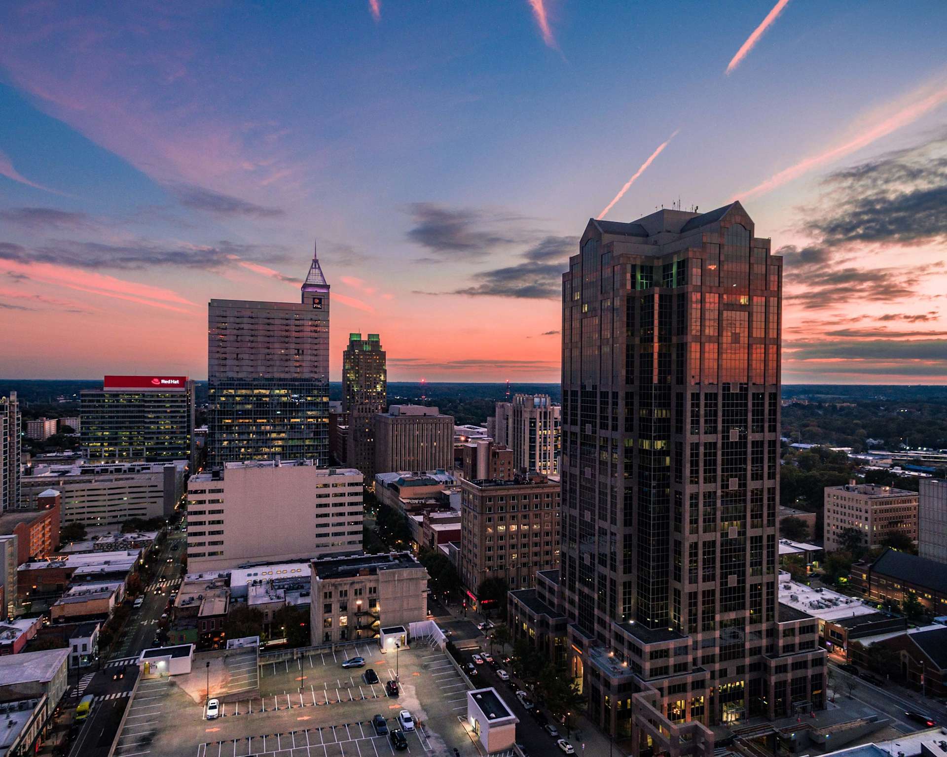 Aerial view of a city skyline at sunset, featuring tall buildings and a colorful sky with clouds.