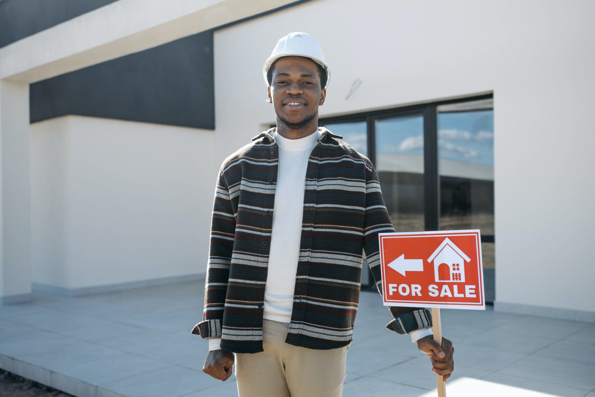 A professional black realtor confidently holding a For Sale signage.