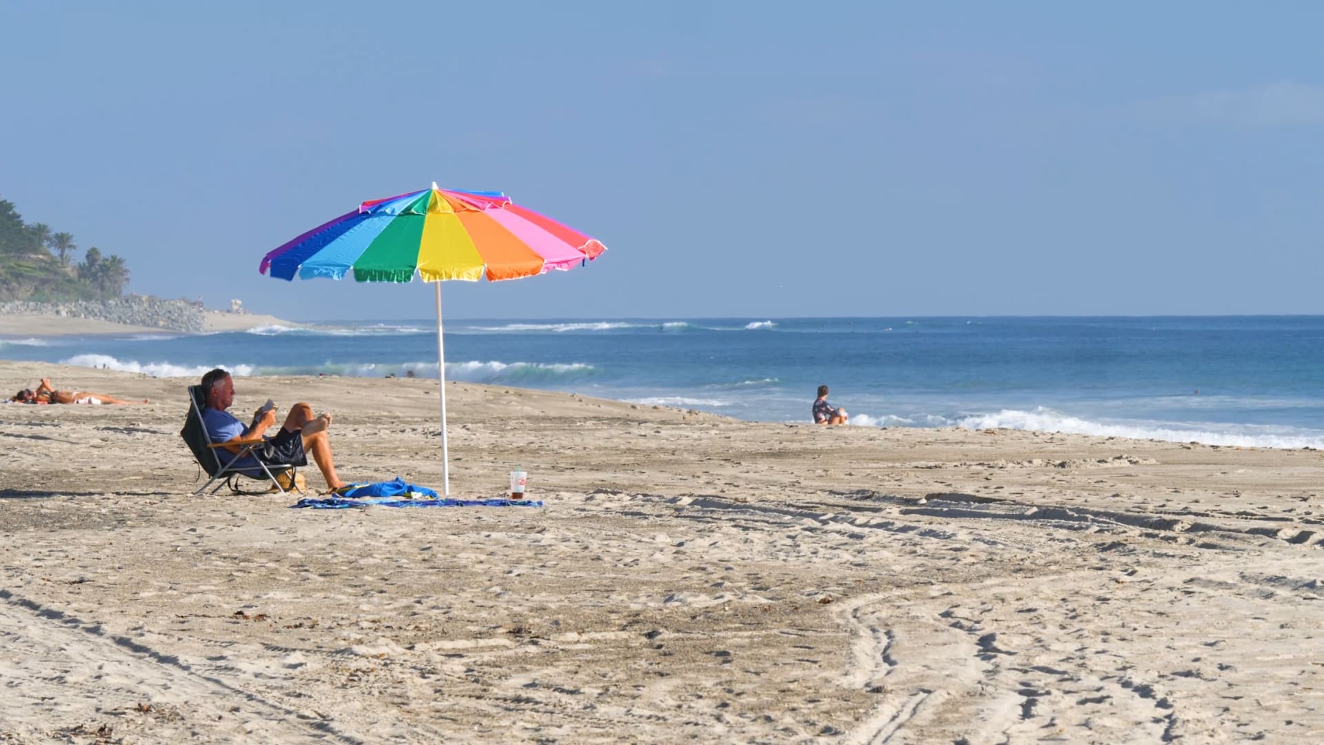 Person sitting in beach chair on the beach with a rainbow umbrella